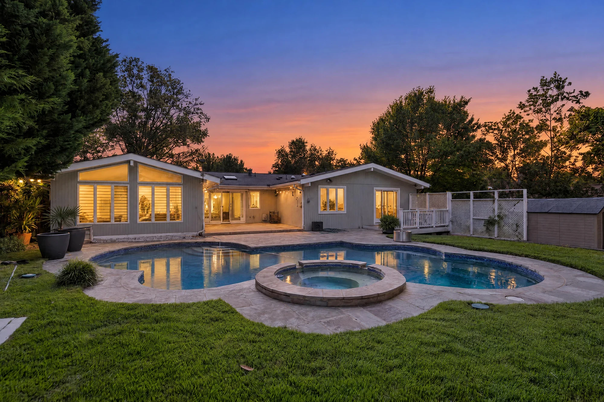 The same backyard pool and spa at dusk with glowing windows and a sunset sky — after virtual twilight by UMedia