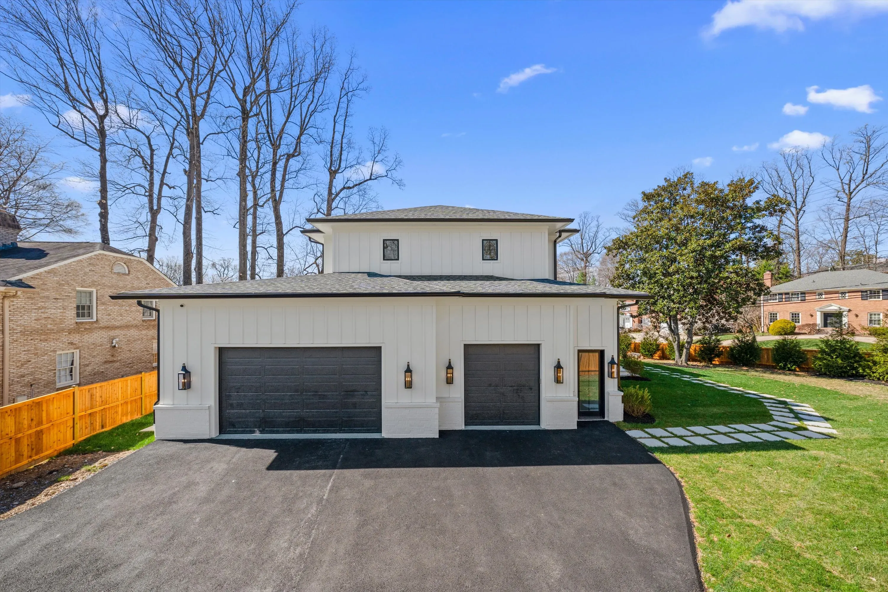 Detached two-bay carriage-style garage with white board-and-batten siding, stone accents, and modern lanterns at luxury Bethesda MD new construction
