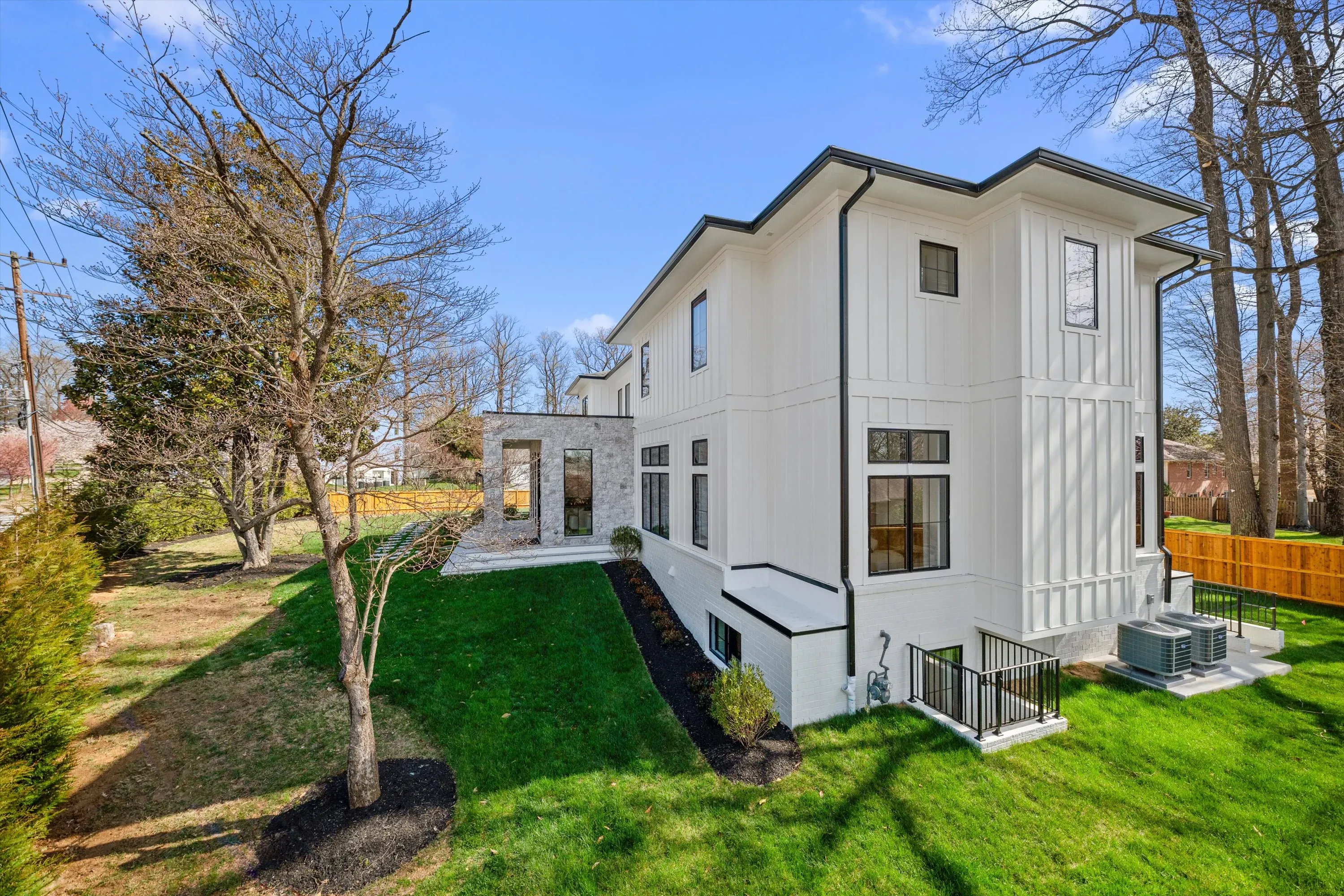Side elevation of three-story new construction home with white board-and-batten siding, fenced lawn, and stone accents in Bethesda MD