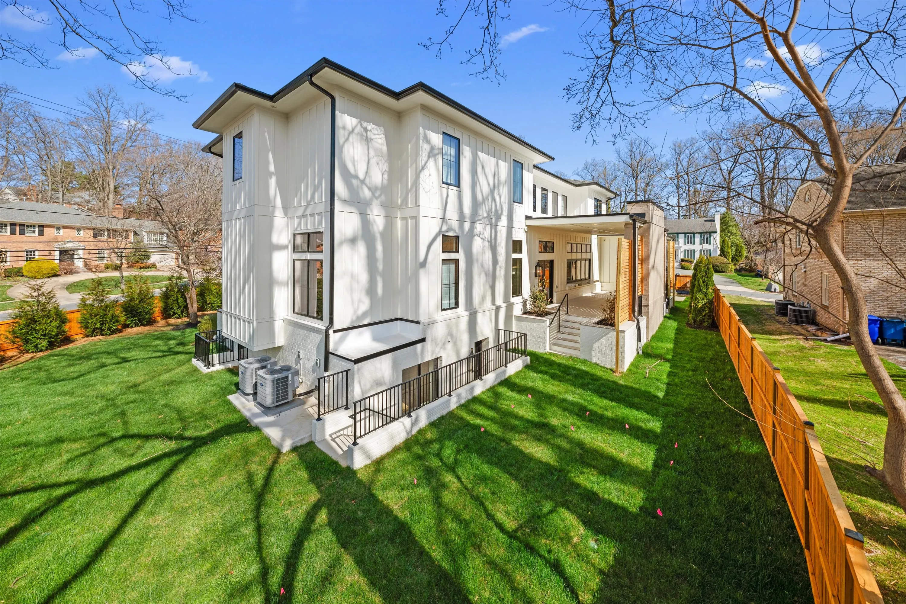 Rear elevation of three-story Bethesda luxury home with covered patio, white board-and-batten siding, and manicured backyard