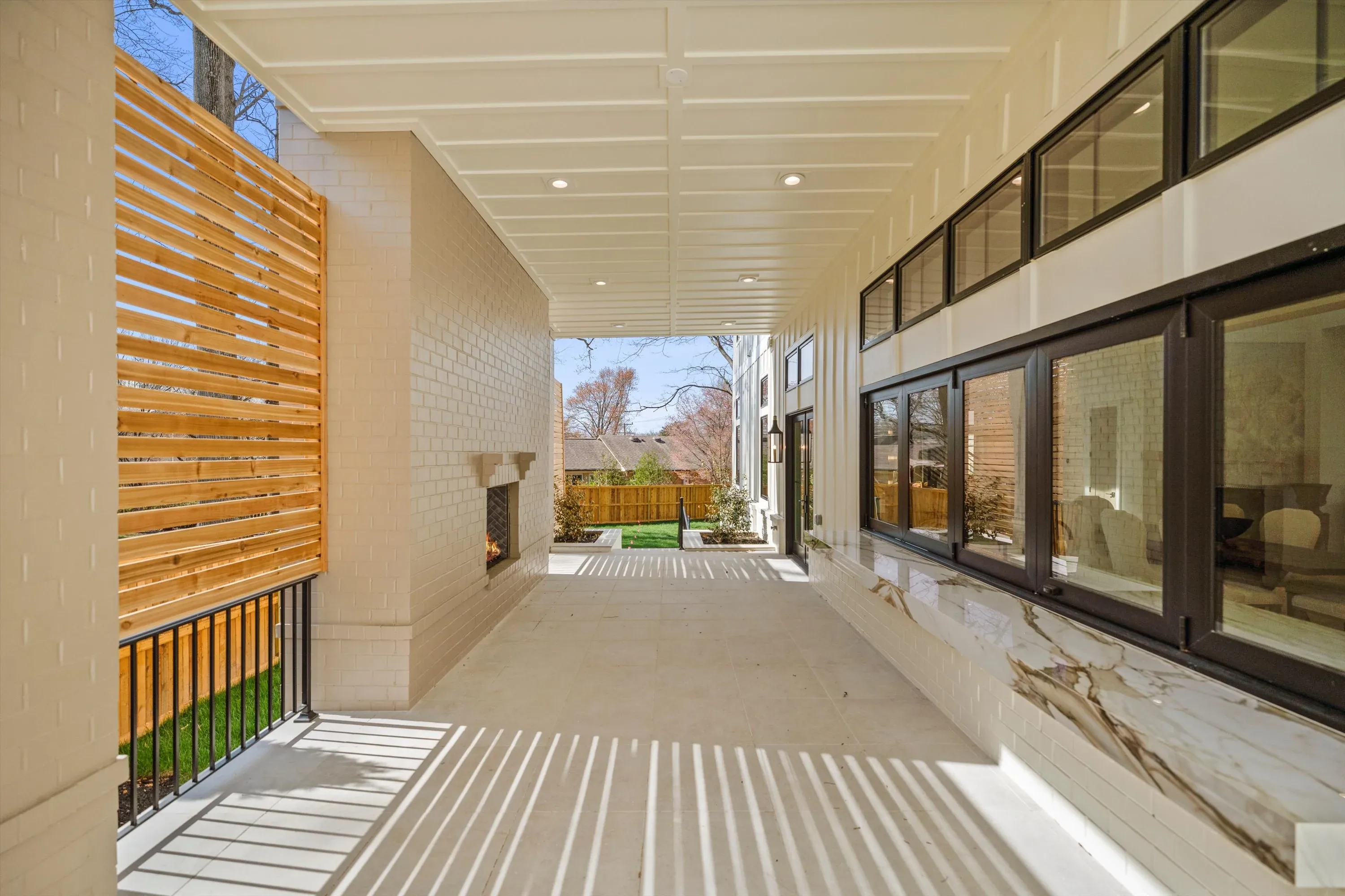 Covered rear patio with outdoor fireplace, calacatta marble bar pass-through, cedar privacy screen, and tongue-and-groove ceiling