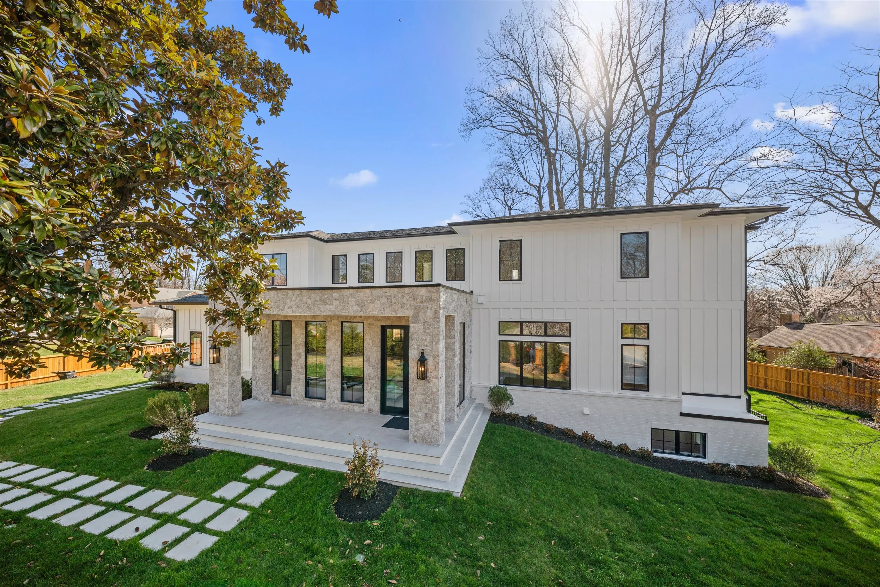 Rear facade of Bethesda luxury home with stone-clad covered patio entry, French doors, board-and-batten siding, and paver walkway