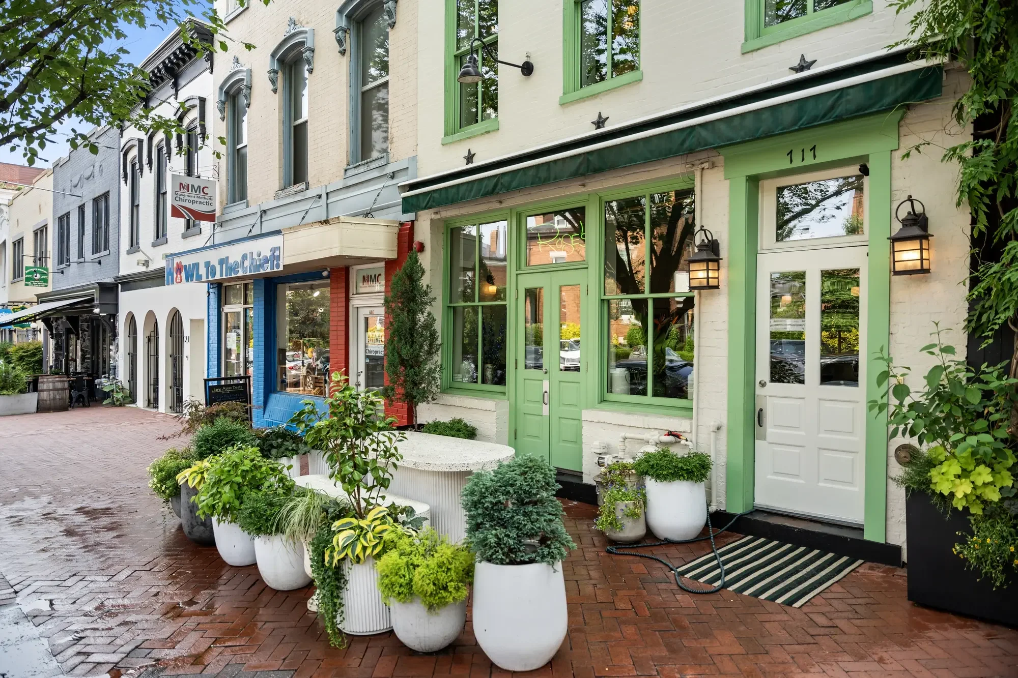Capitol Hill storefront streetscape with green-trimmed shopfront and wet brick sidewalk near Barracks Row, Washington, DC