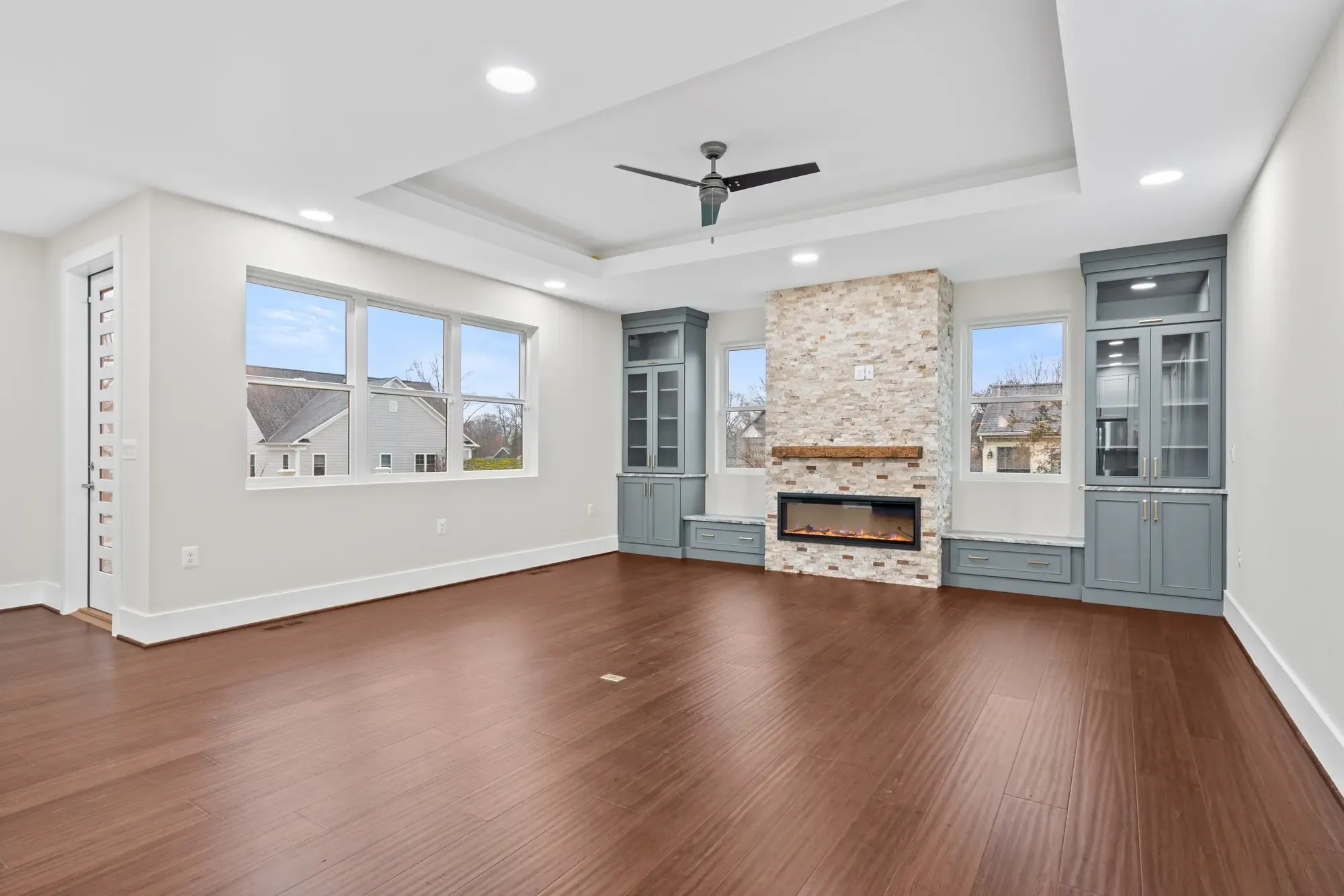 Spacious family room with tray ceiling, stone fireplace, and blue built-in cabinetry