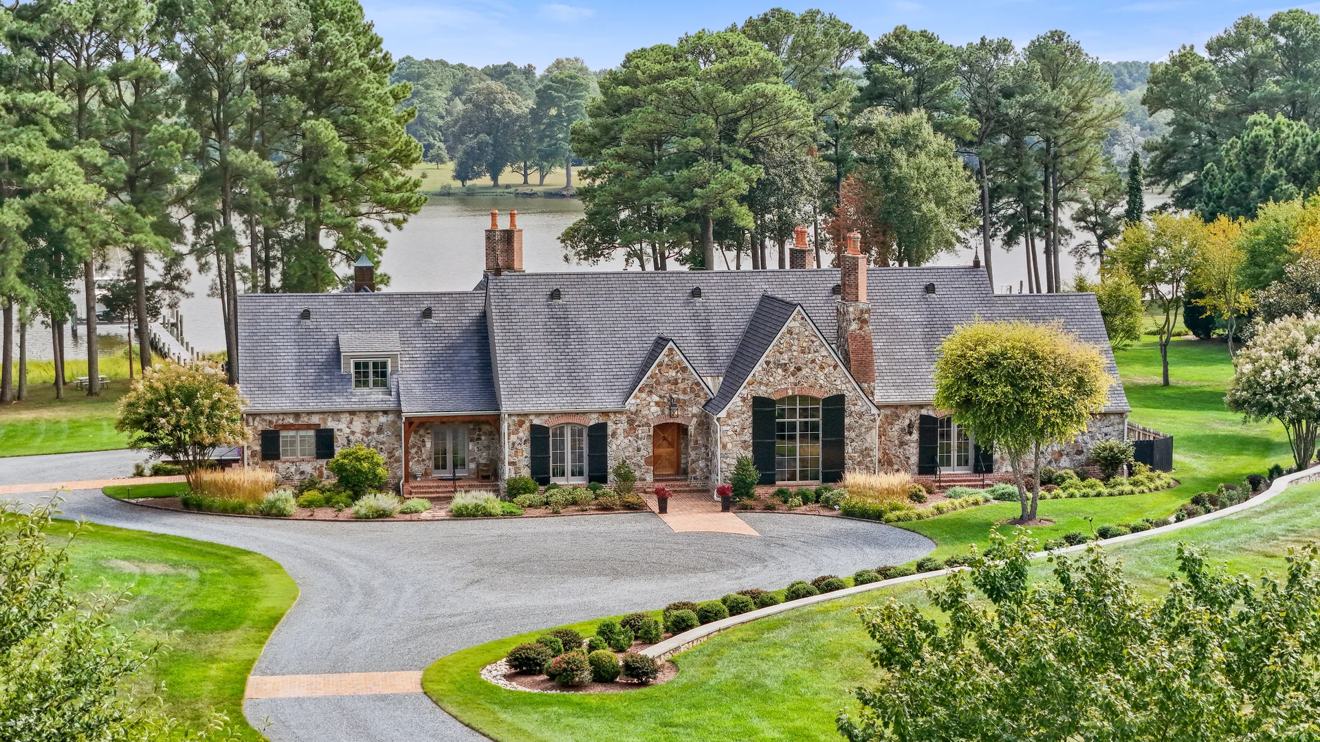 Aerial drone photography of a stone lakefront estate with manicured grounds and tree-lined driveway in Potomac Maryland by Umedia