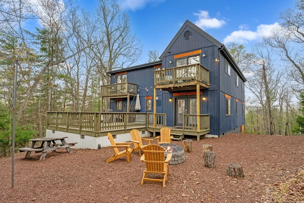 Daytime photo of a two-story home with wraparound deck and fire-pit seating area — before virtual twilight conversion