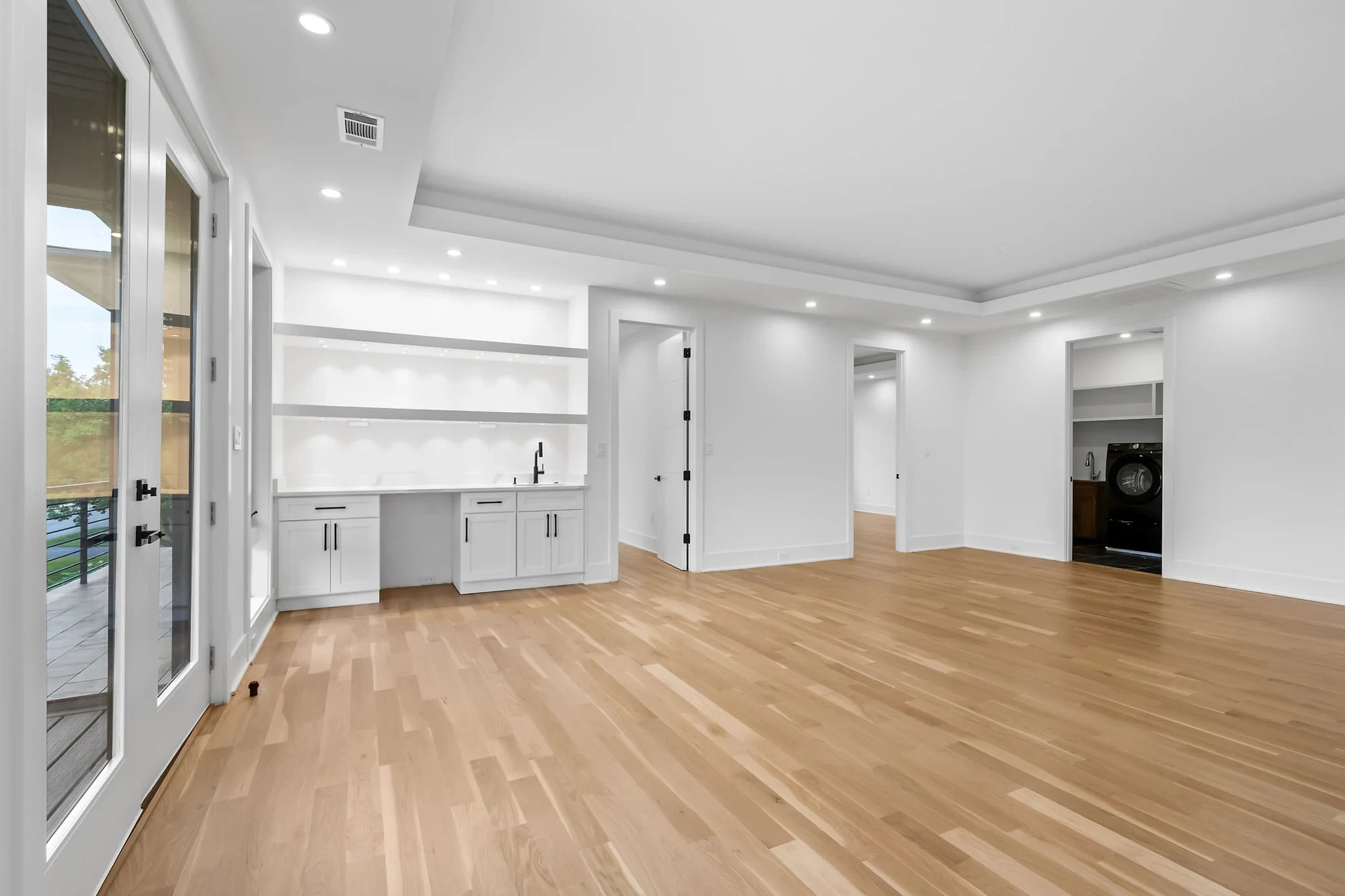 Vacant family room with hardwood floors, a built-in wet bar, and French doors to the deck — before virtual staging