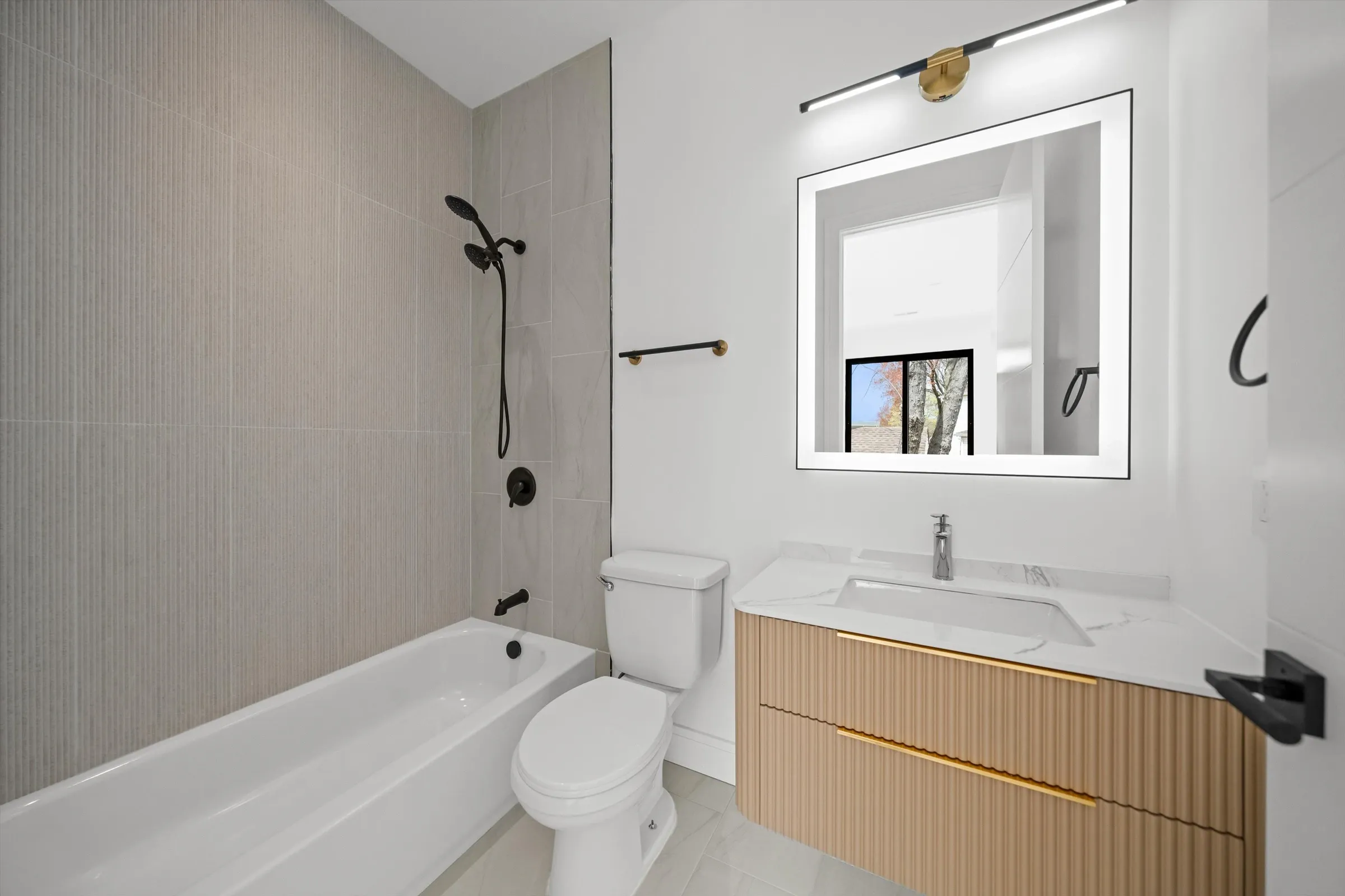 Bathroom with gray linear tile shower-tub combo, LED mirror, floating oak vanity with gold accent strip, and chrome faucet