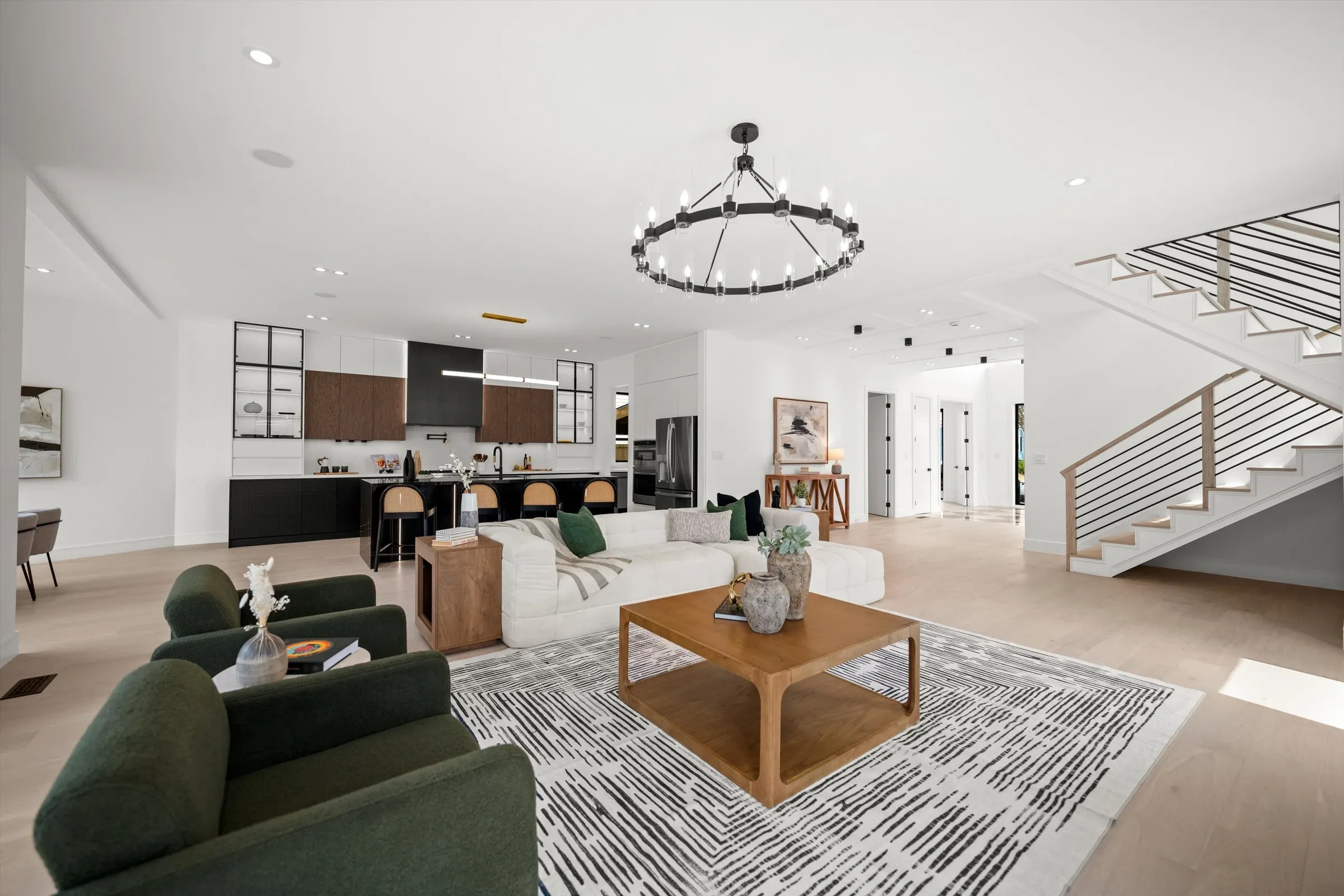 Open-concept main level with living area, iron chandelier, designer kitchen with black island, modern staircase, and light oak floors throughout