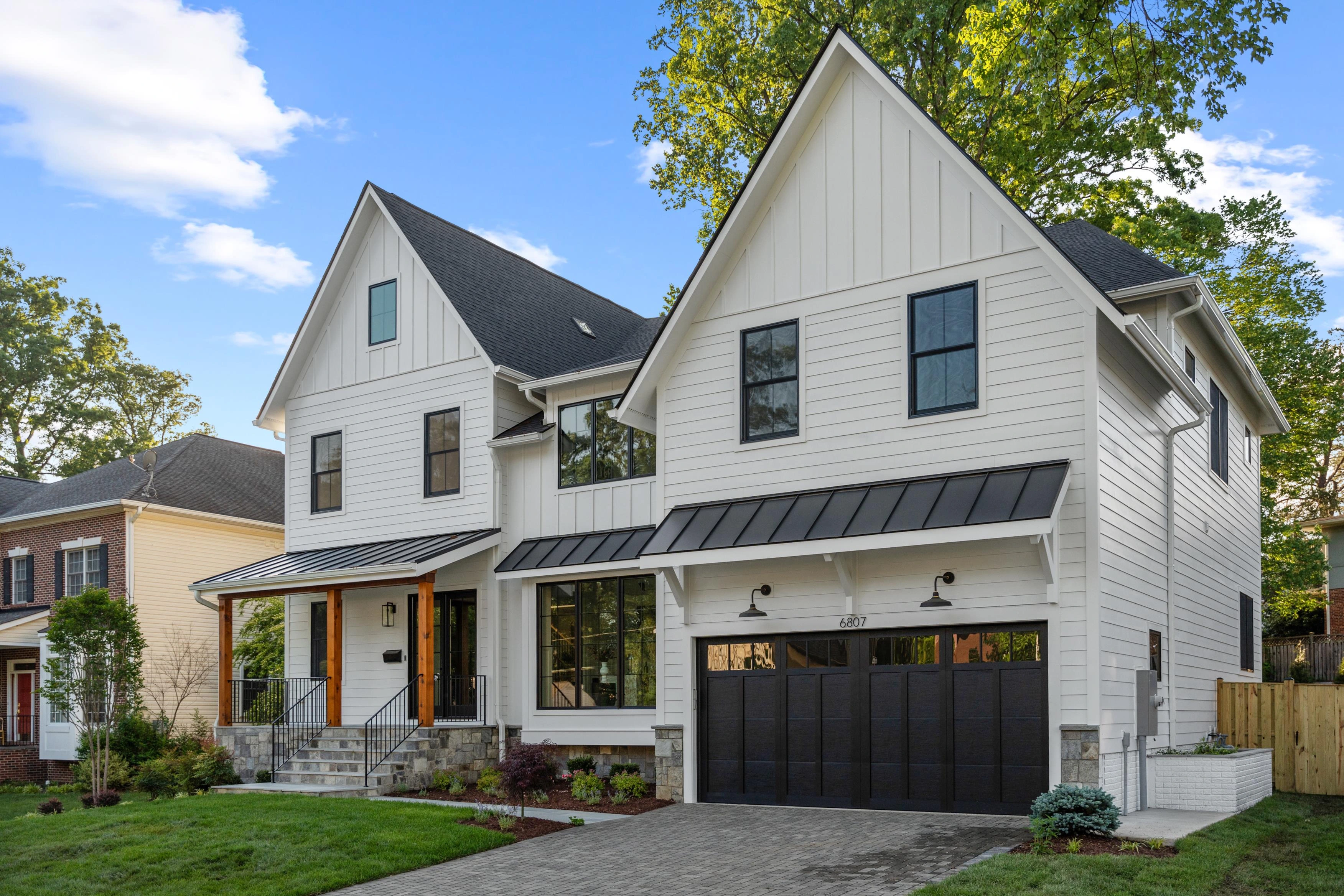 New construction luxury home with white board-and-batten siding, black metal awnings, and cedar porch columns
