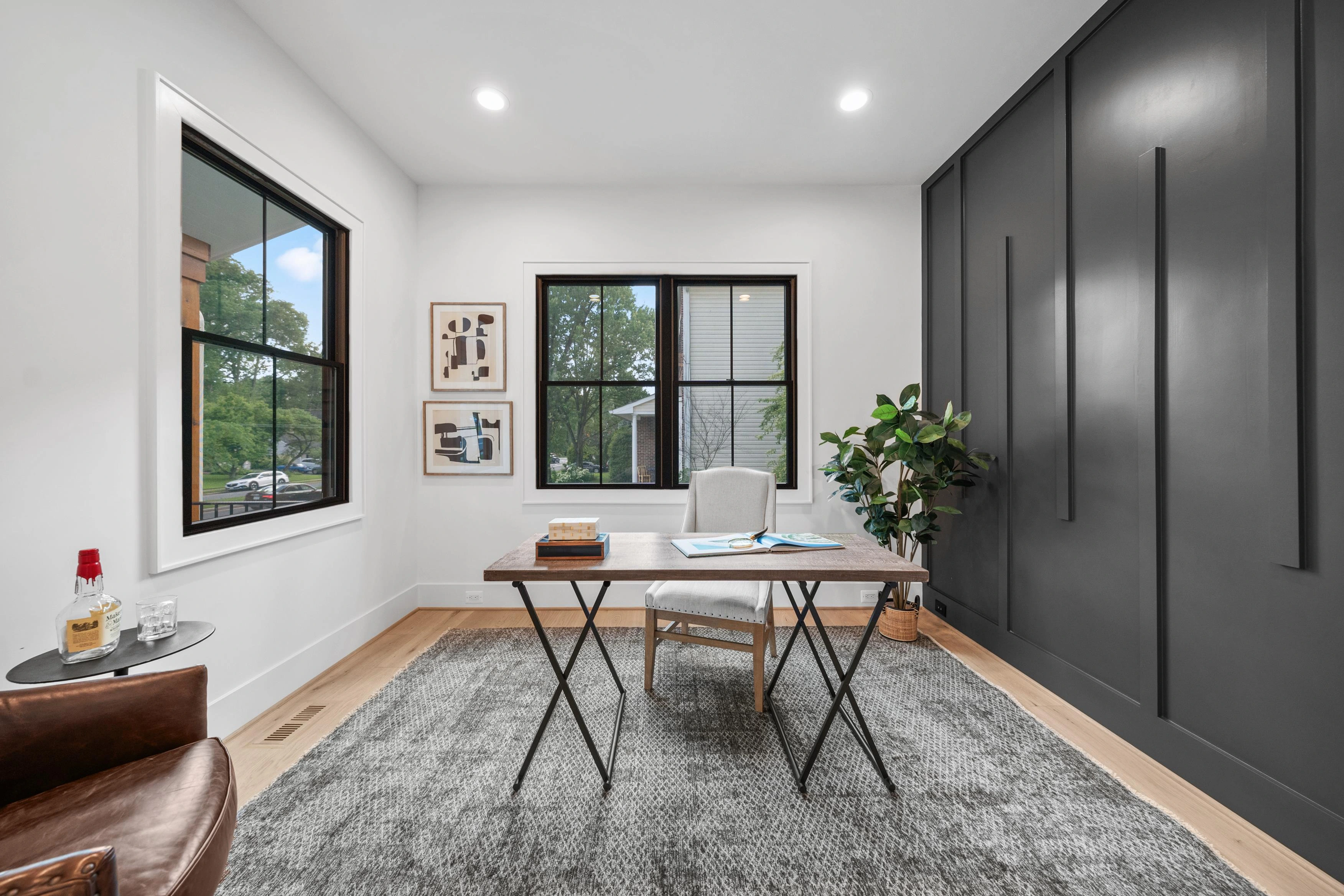 Modern home office with dark accent wall paneling, natural light, and designer furnishings
