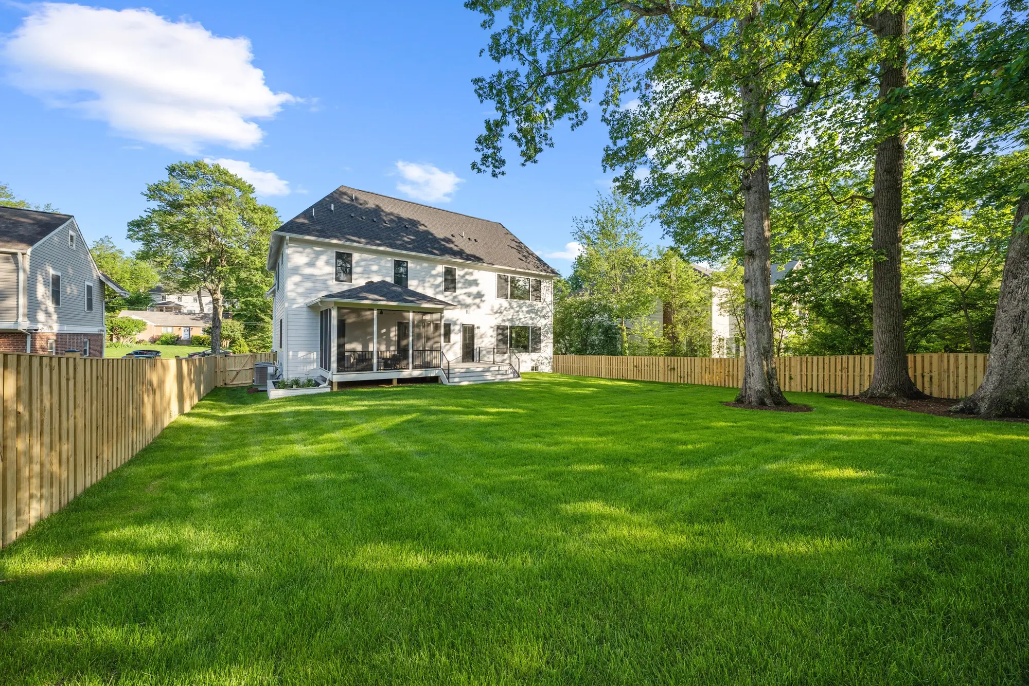 Large fenced backyard with green lawn, screened porch, and mature oak trees