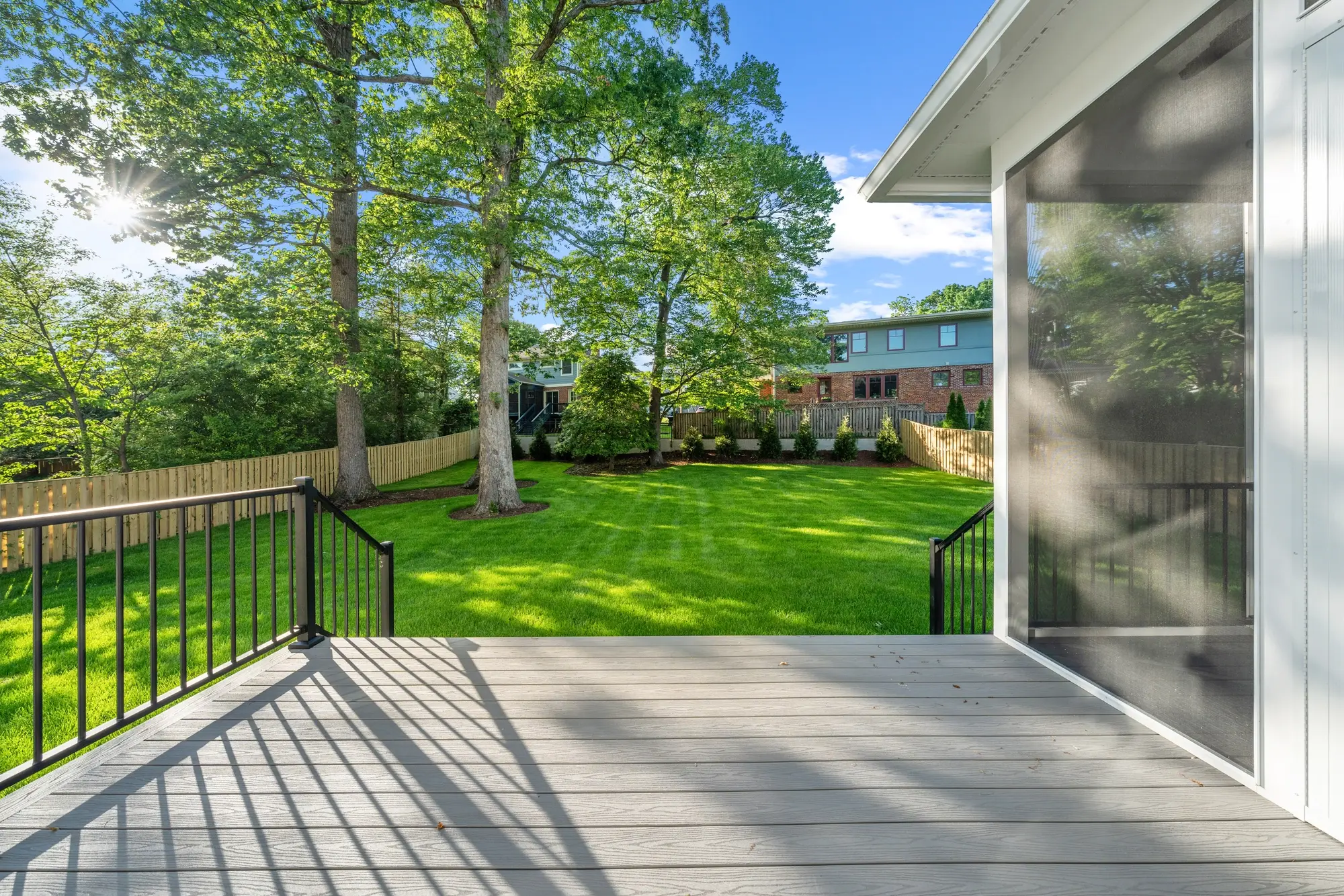 Composite deck with metal railing overlooking green fenced backyard with mature trees