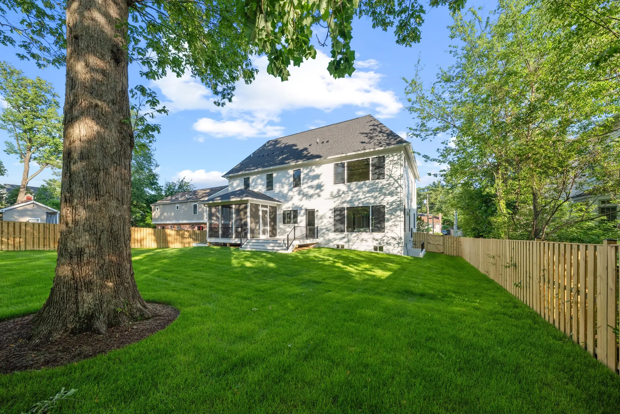 Wide view of custom home rear exterior with screened porch and spacious fenced yard