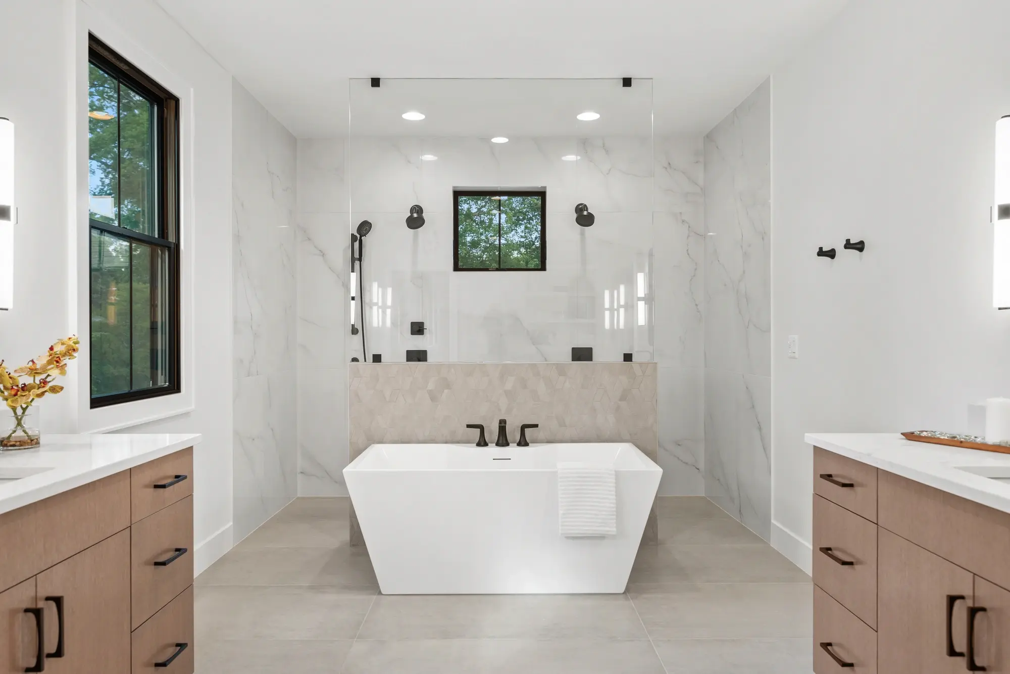 Master bathroom with freestanding tub, dual vanities, marble tile, and frameless glass shower