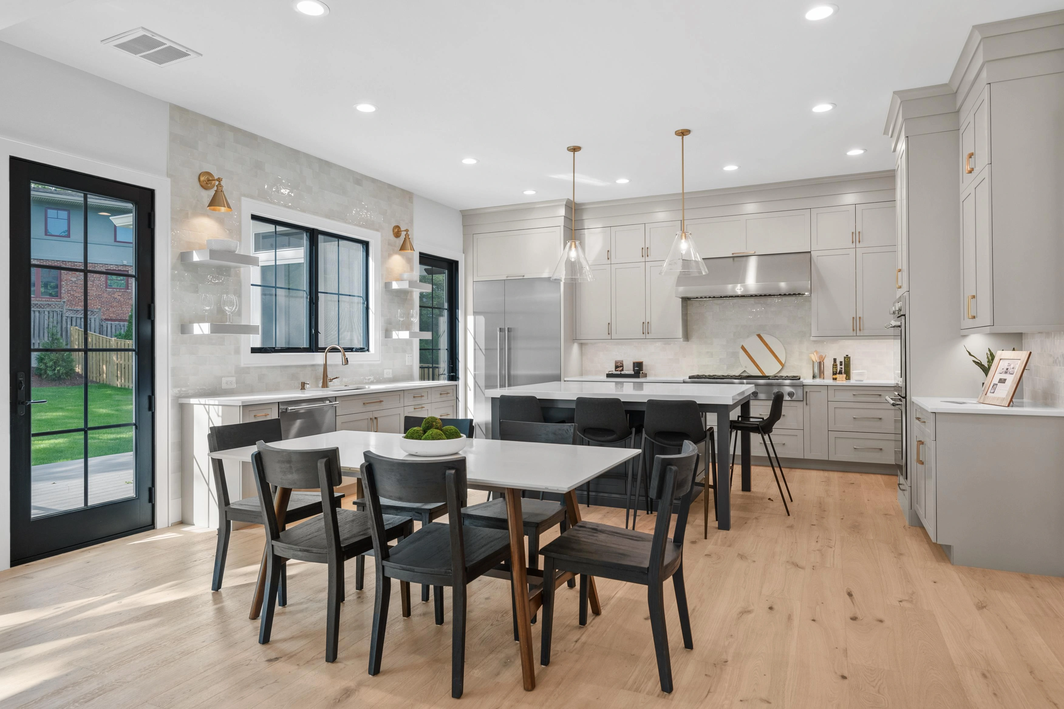 Open kitchen and dining area with sage green cabinetry, brass hardware, and pendant lighting