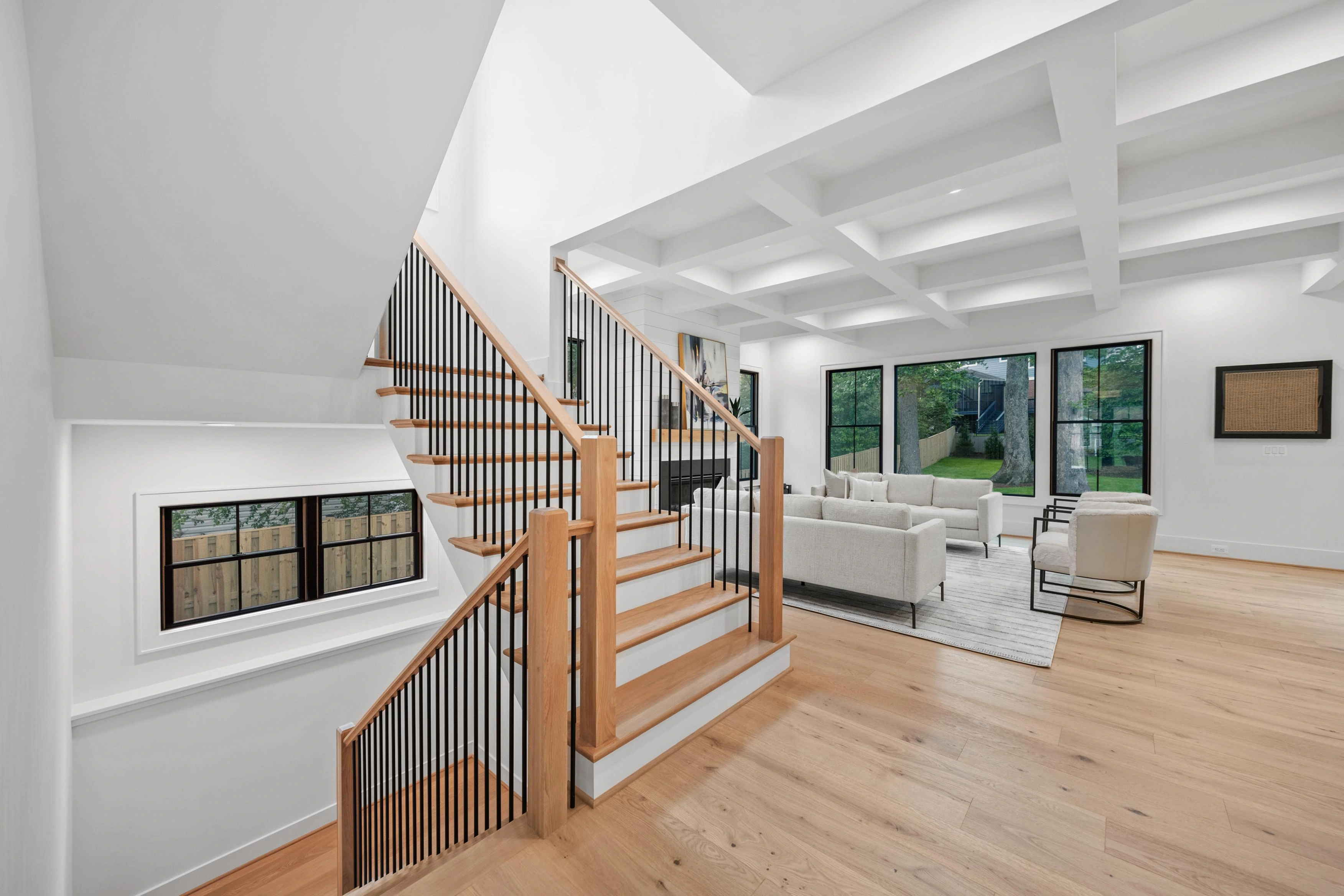 Open staircase with oak treads and iron spindles leading to living room with coffered ceiling