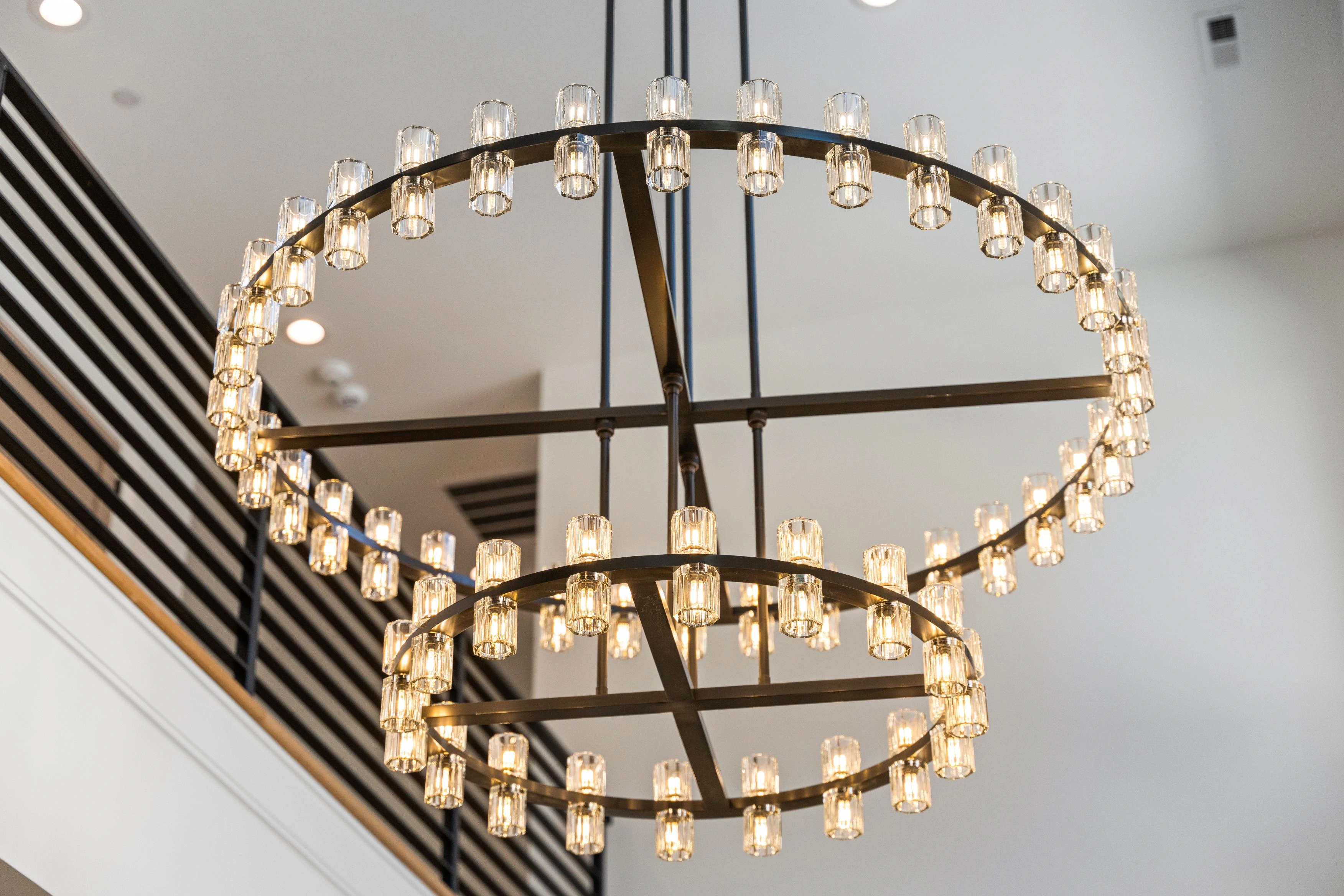 Statement double-ring crystal chandelier in double-height foyer with iron staircase railing