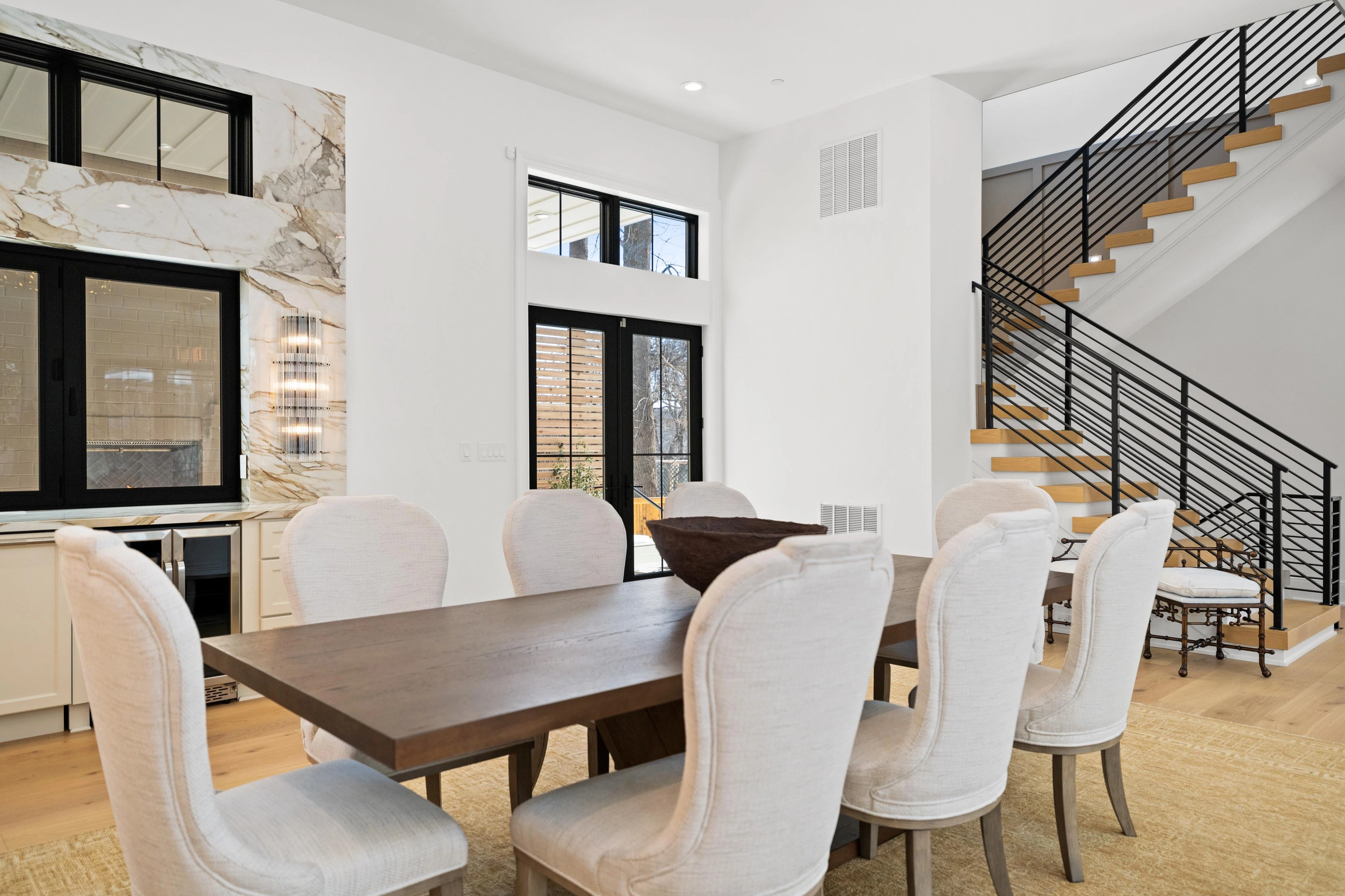 Formal dining area with eight-seat table, open staircase with iron railing, and kitchen pass-through window