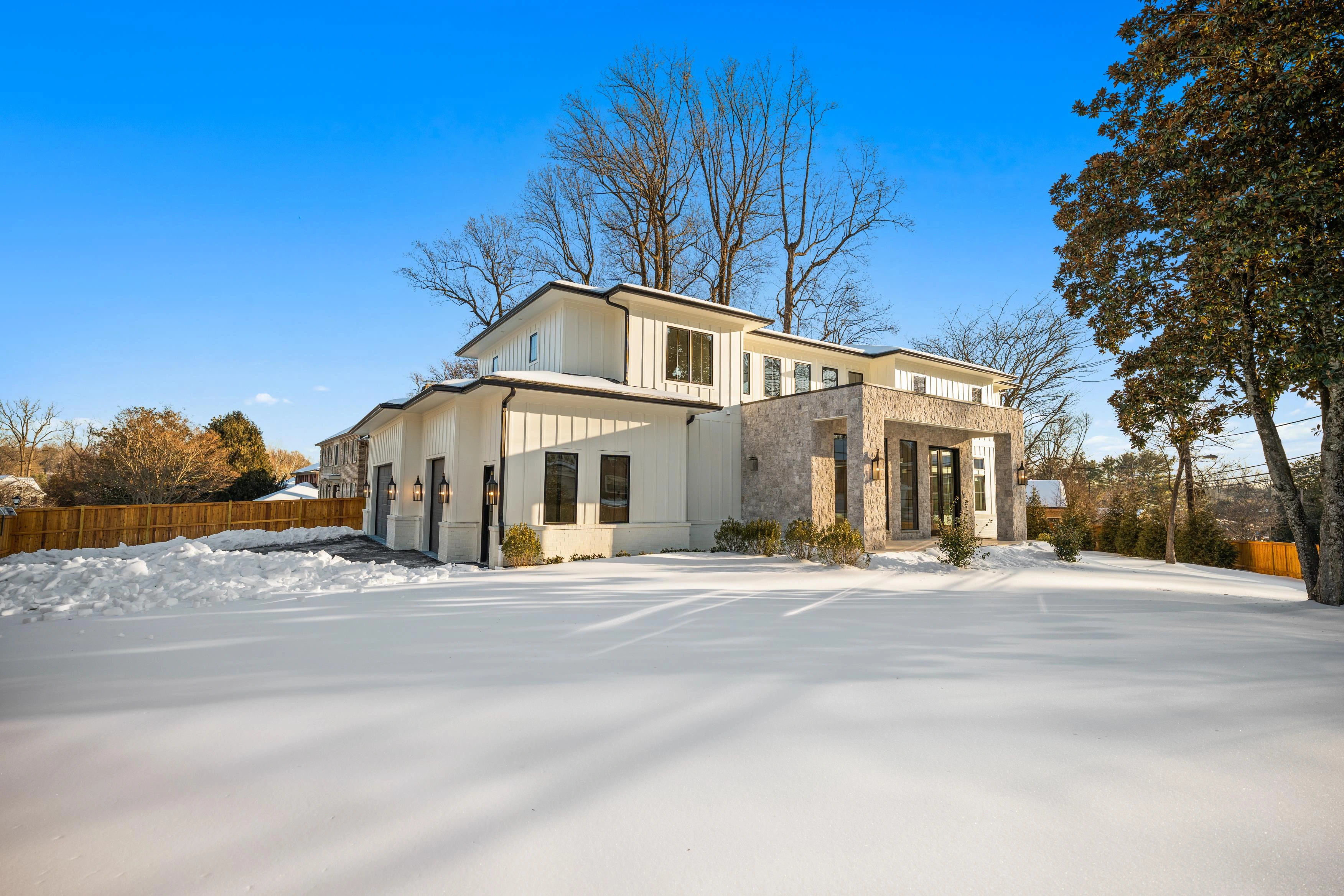 Modern luxury new construction home with white board-and-batten siding, stone entry, and black-framed windows in snow-covered Bethesda MD