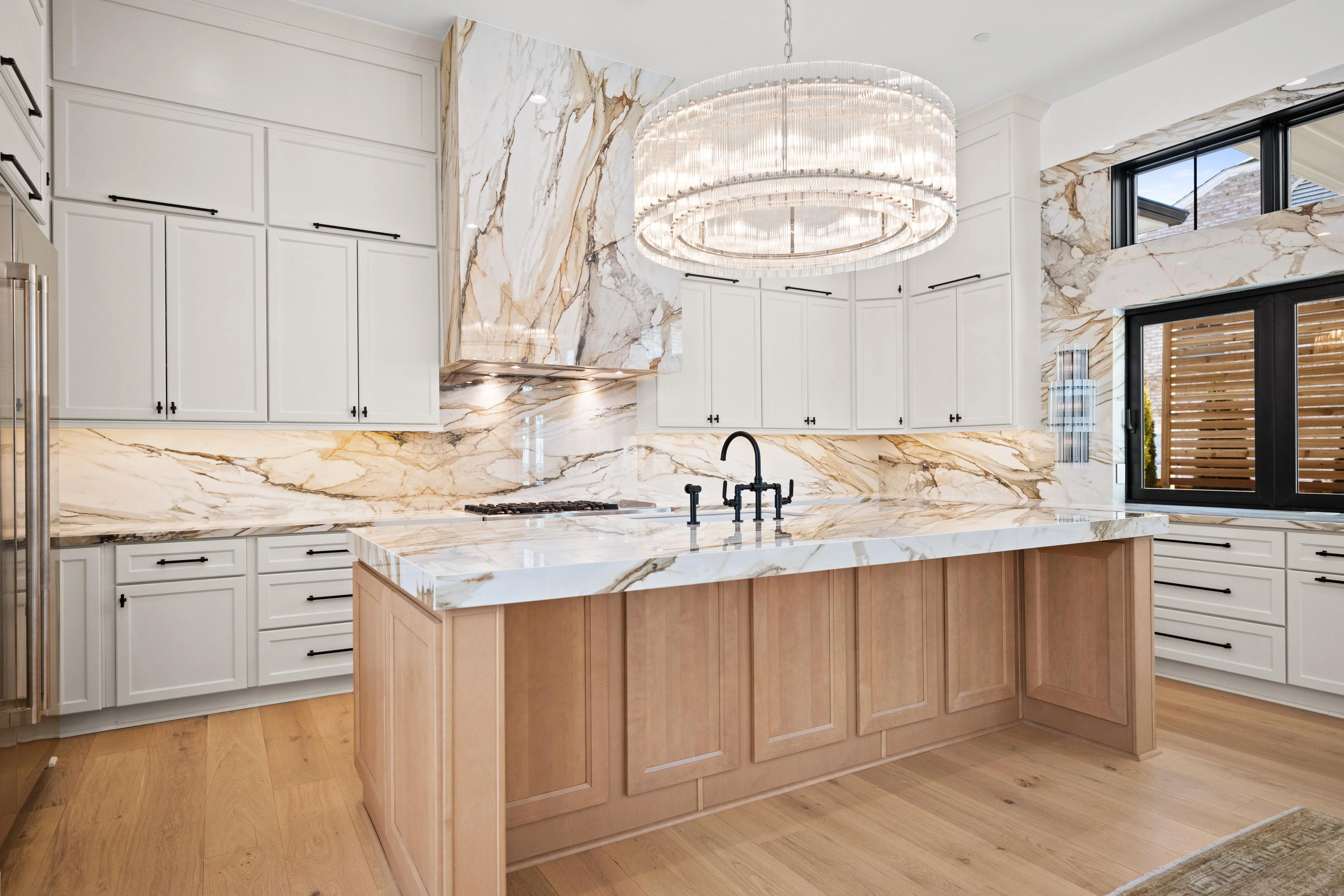 Kitchen island close-up showing book-matched calacatta marble countertop and black bridge faucet