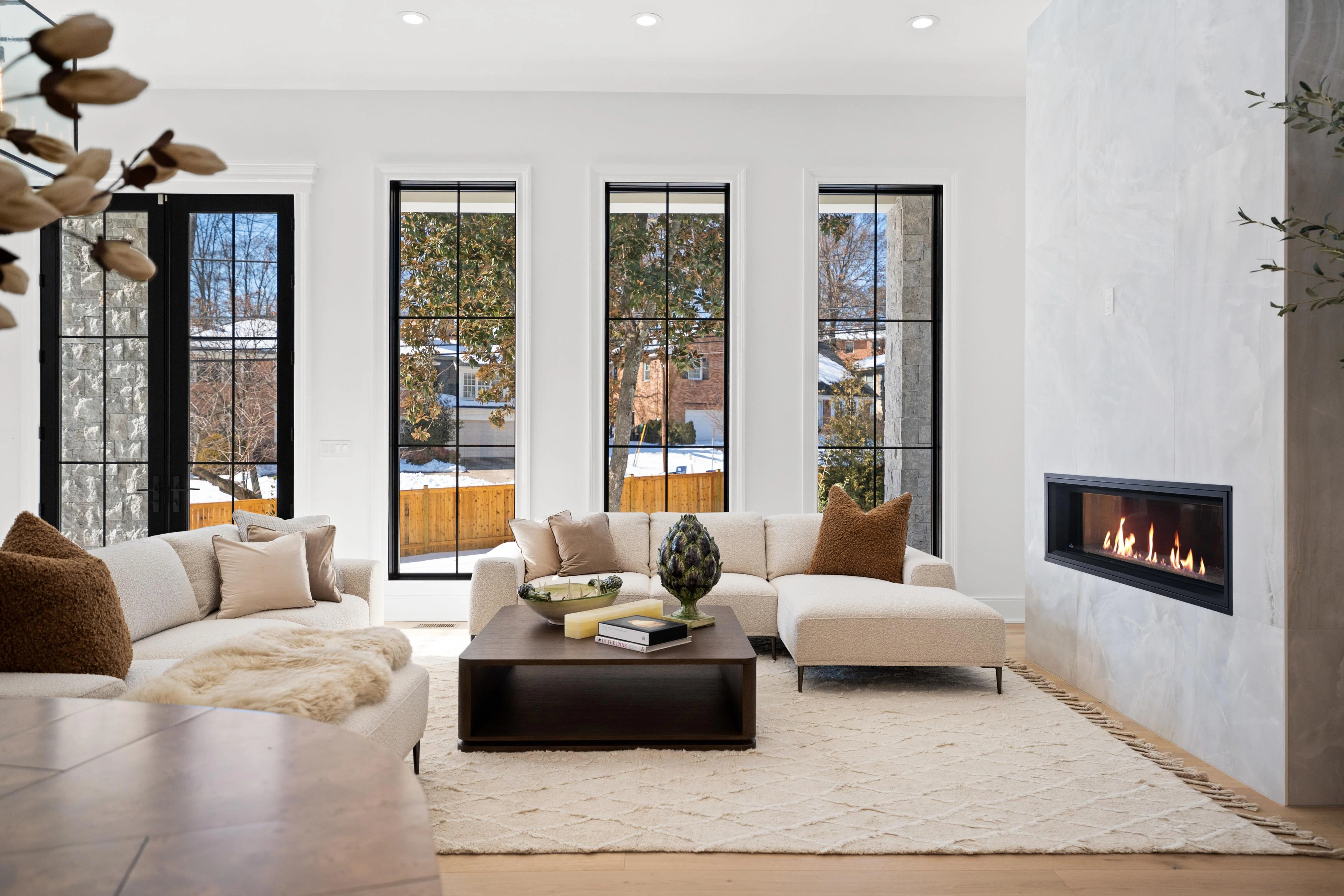 Living room with floor-to-ceiling black-framed windows, linear gas fireplace, and designer furniture