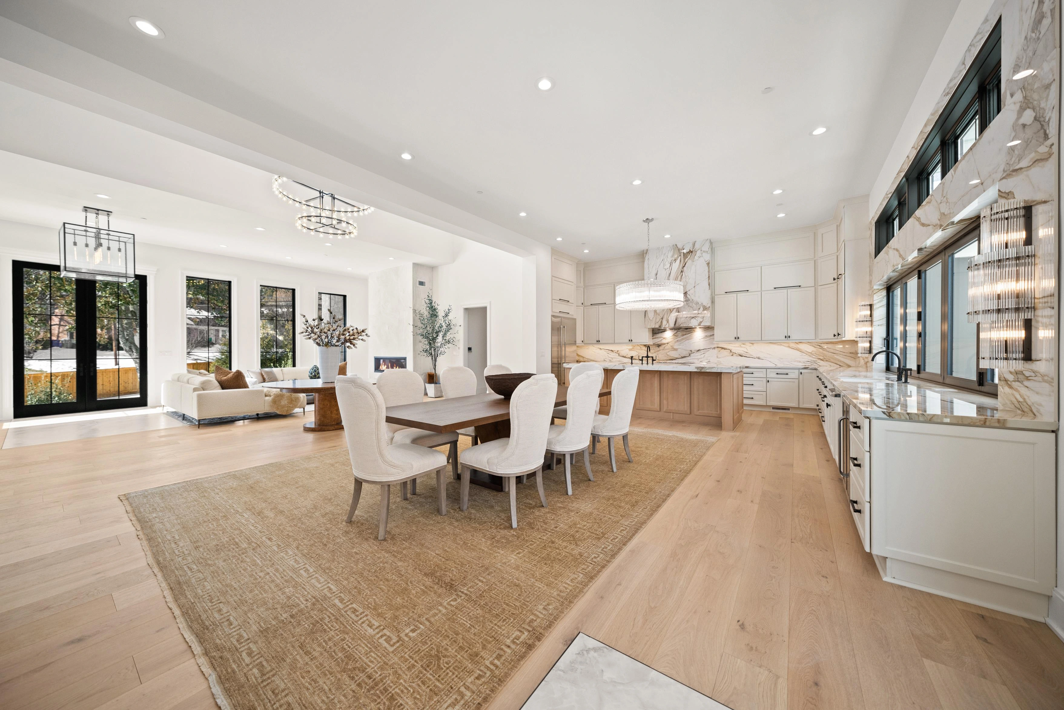 Wide view of open-concept living, dining, and kitchen with calacatta marble, crystal chandelier, and oak island