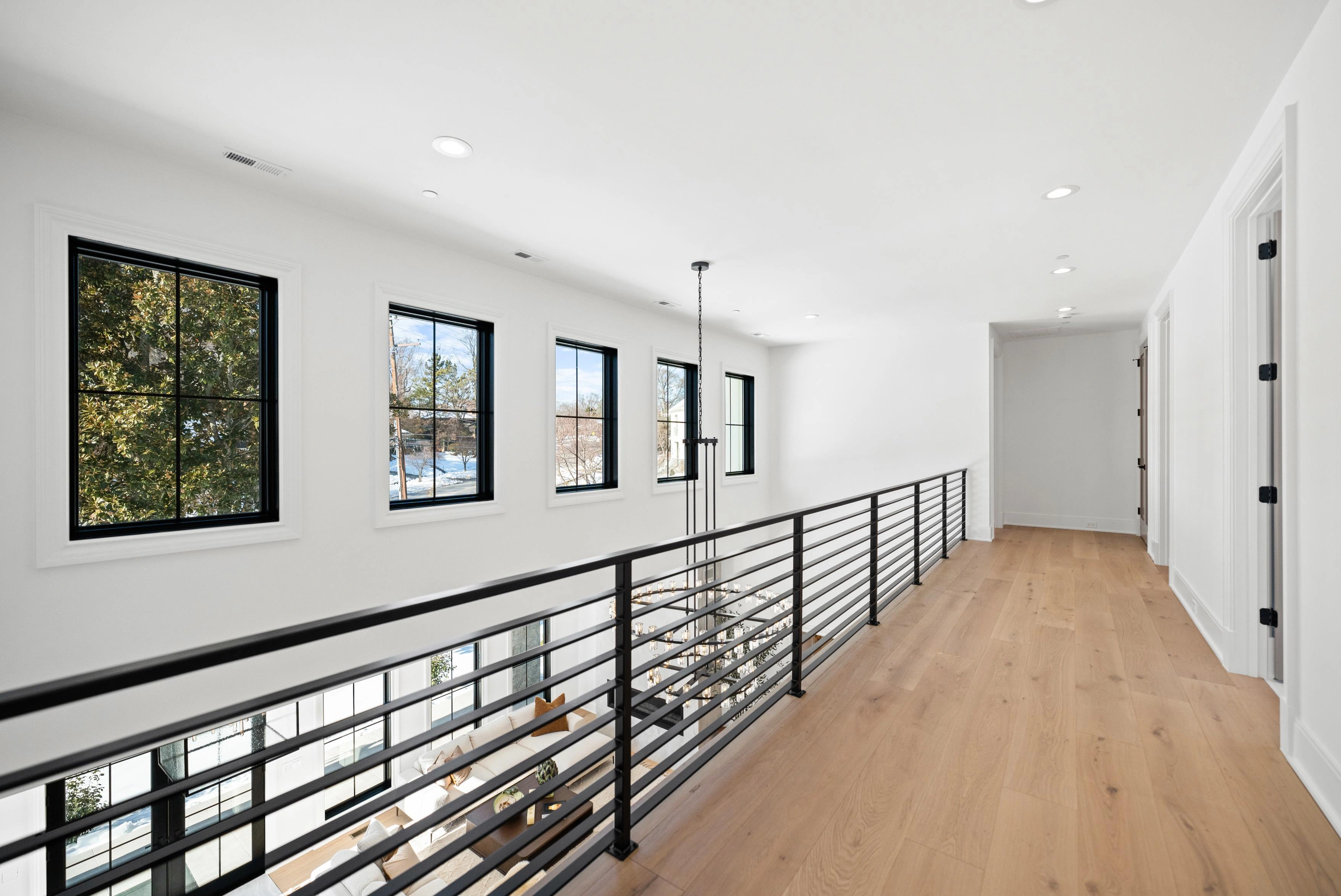 Second-floor hallway with iron horizontal railing overlooking double-height great room and chandelier