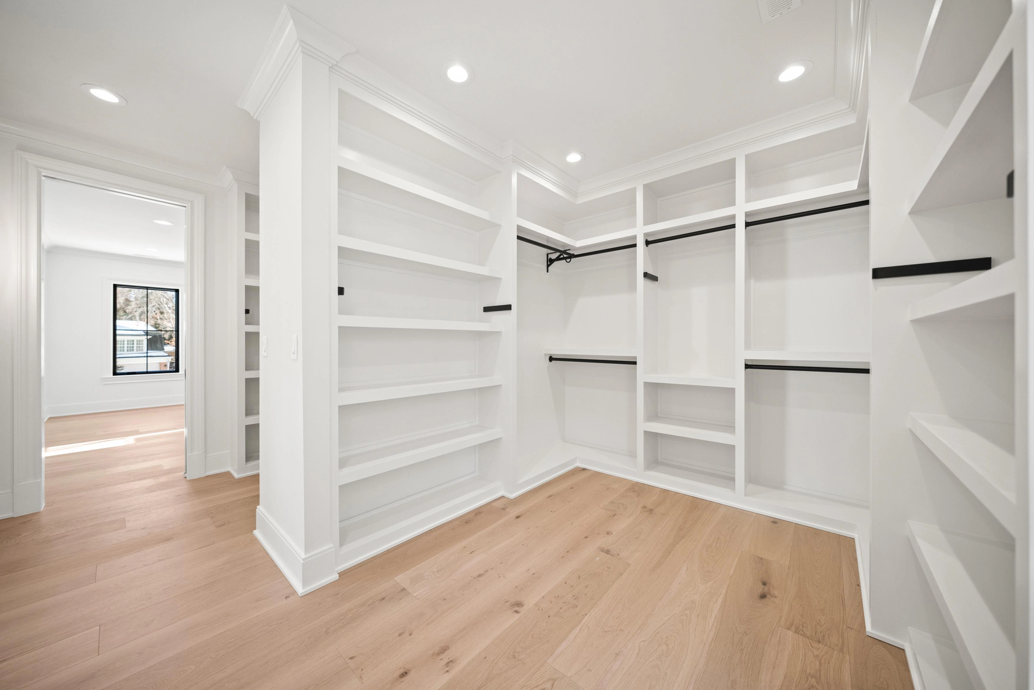 Custom walk-in closet with built-in shelving, crown molding, and black hanging rods