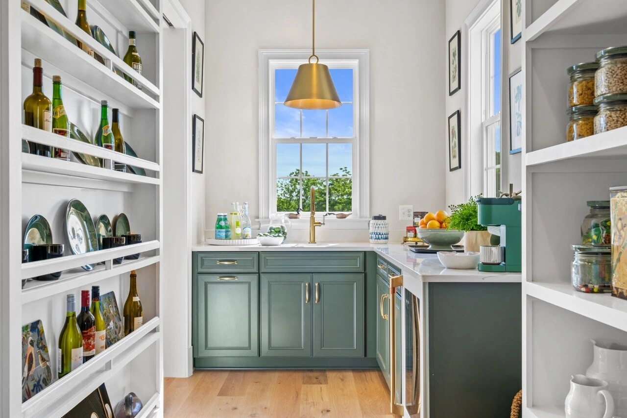 Butler pantry with sage green cabinets, brass hardware, and open shelving in country estate
