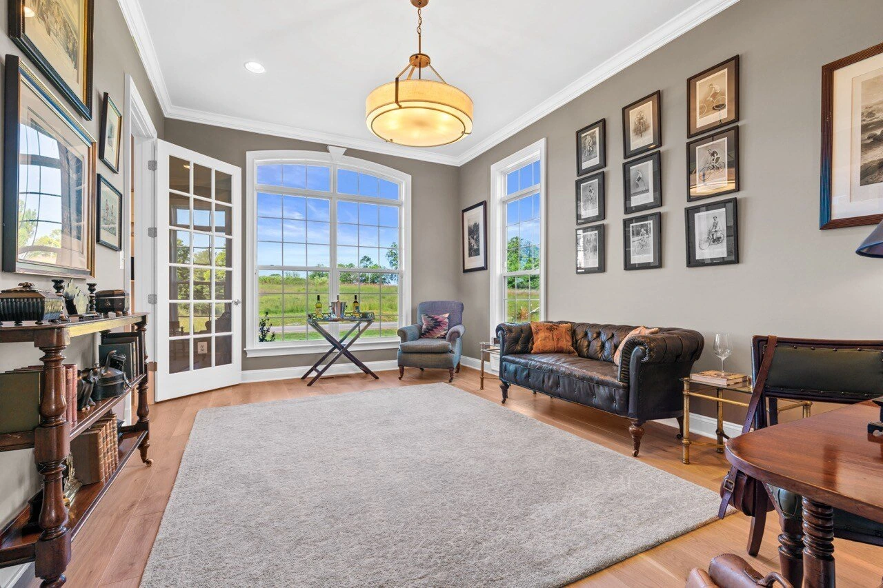 Study with leather Chesterfield sofa, gallery wall, French doors, and countryside views