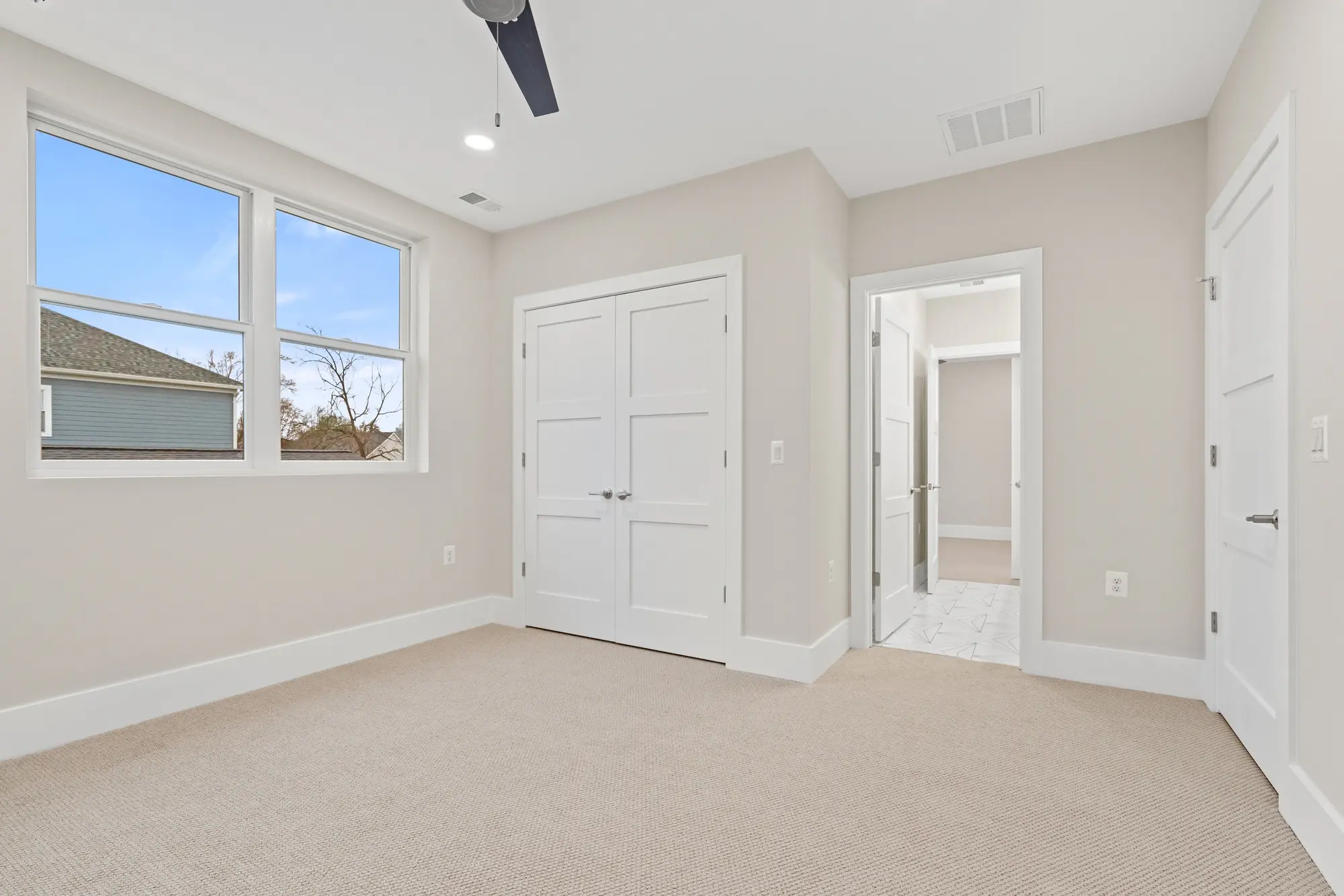Bright bedroom with large windows, carpet flooring, and ceiling fan