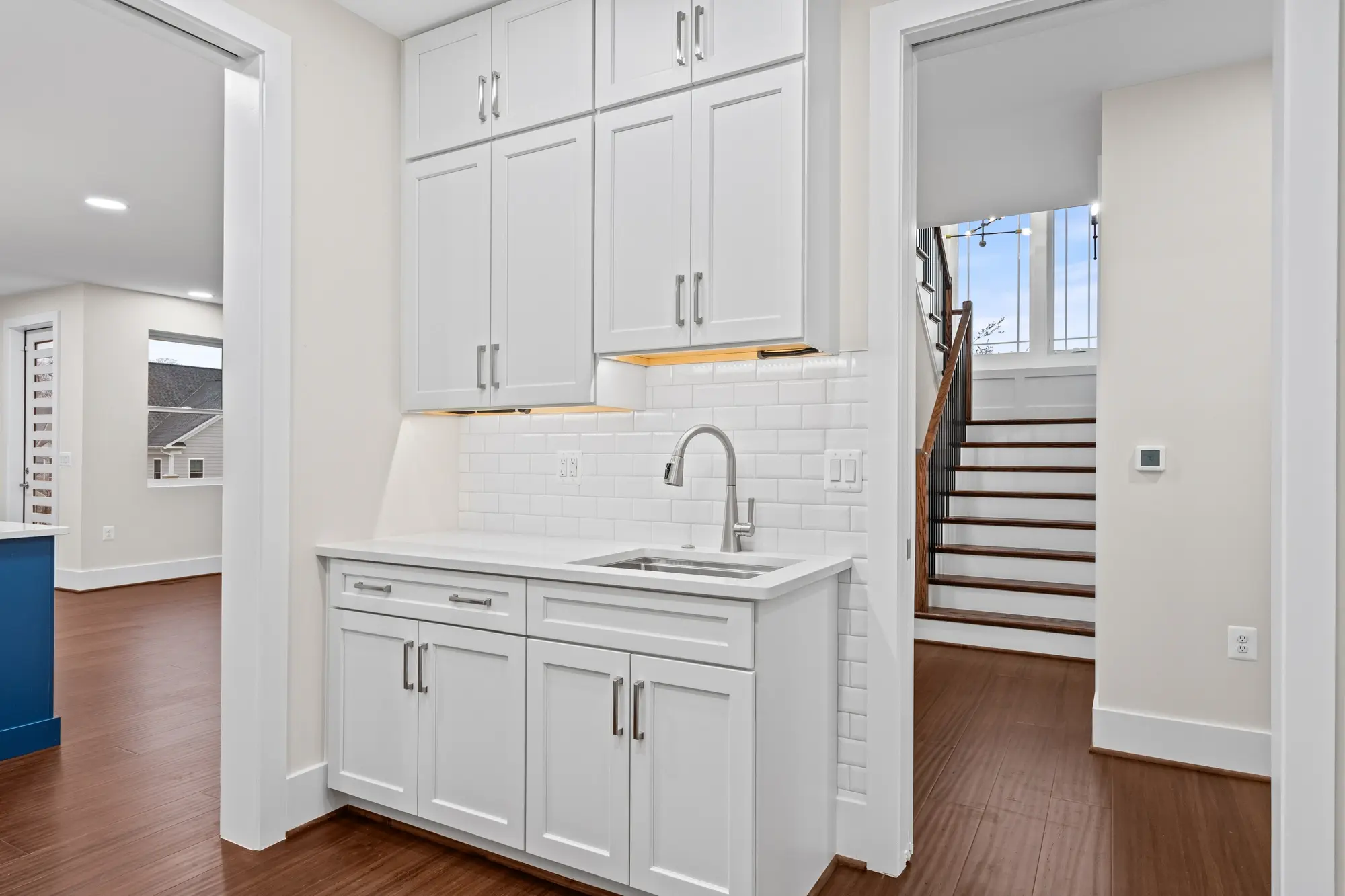 Butler's pantry with white shaker cabinets, subway tile backsplash, and staircase