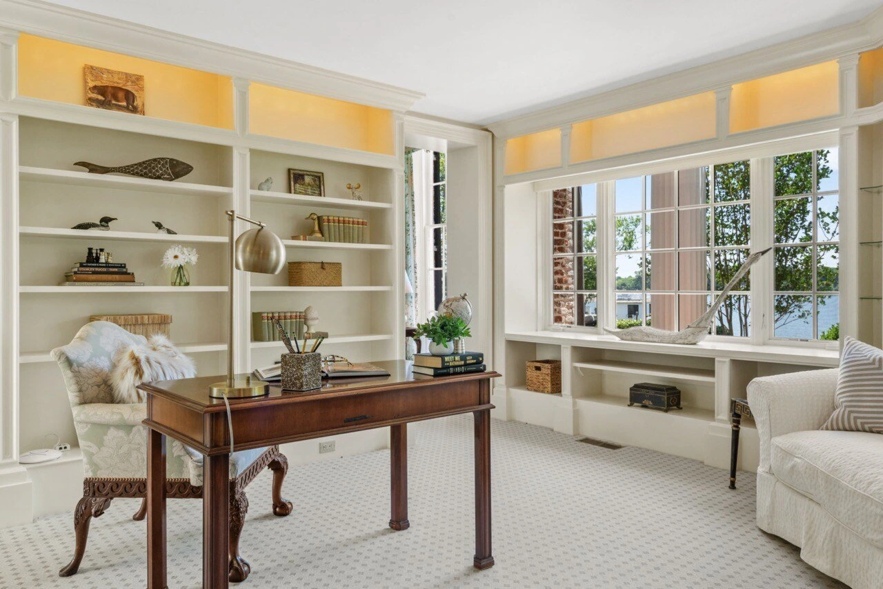 Home office with built-in bookshelves, antique desk, and waterfront window seat