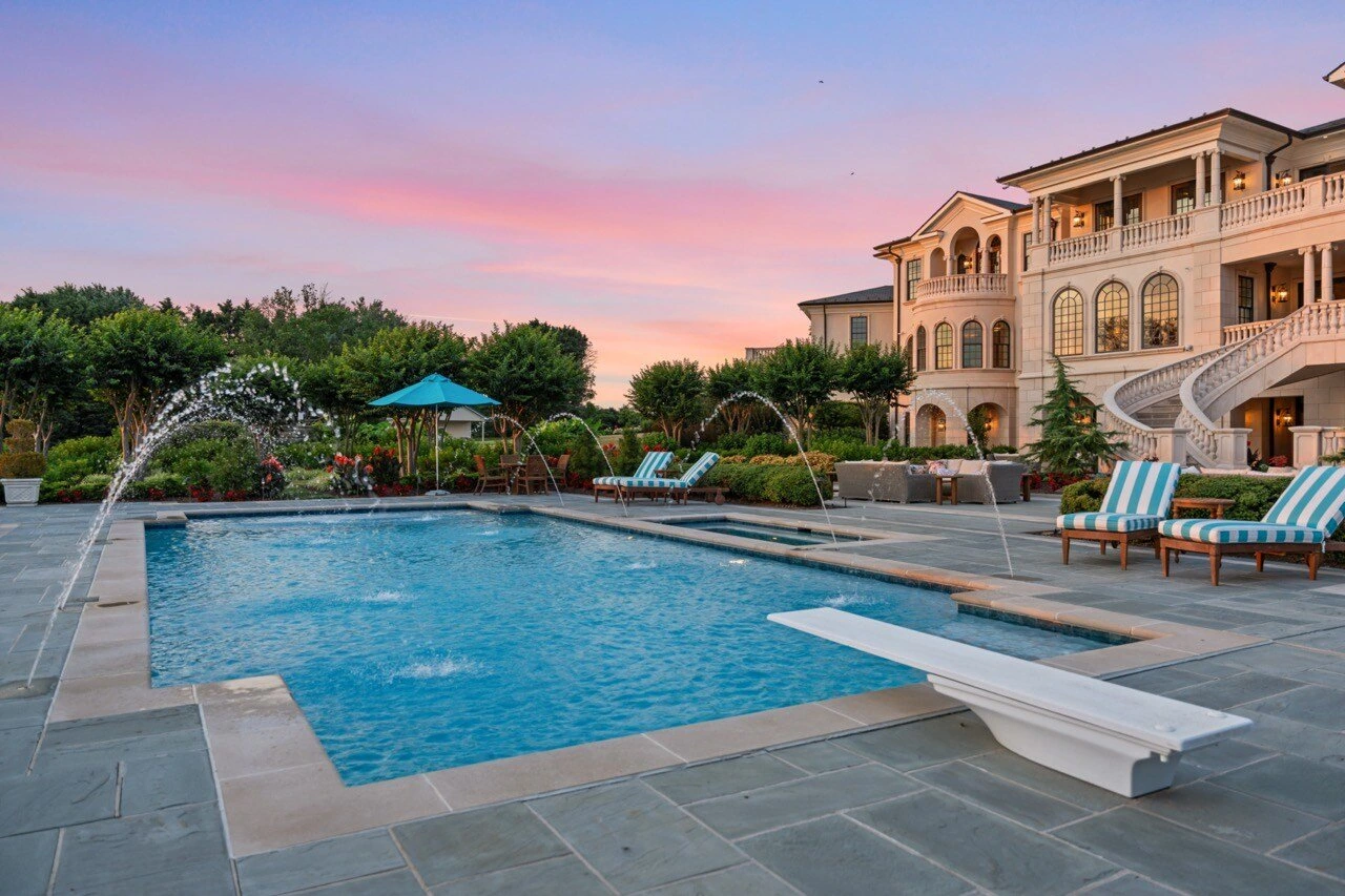 Luxury estate pool and mansion at twilight with fountain jets and blue sky