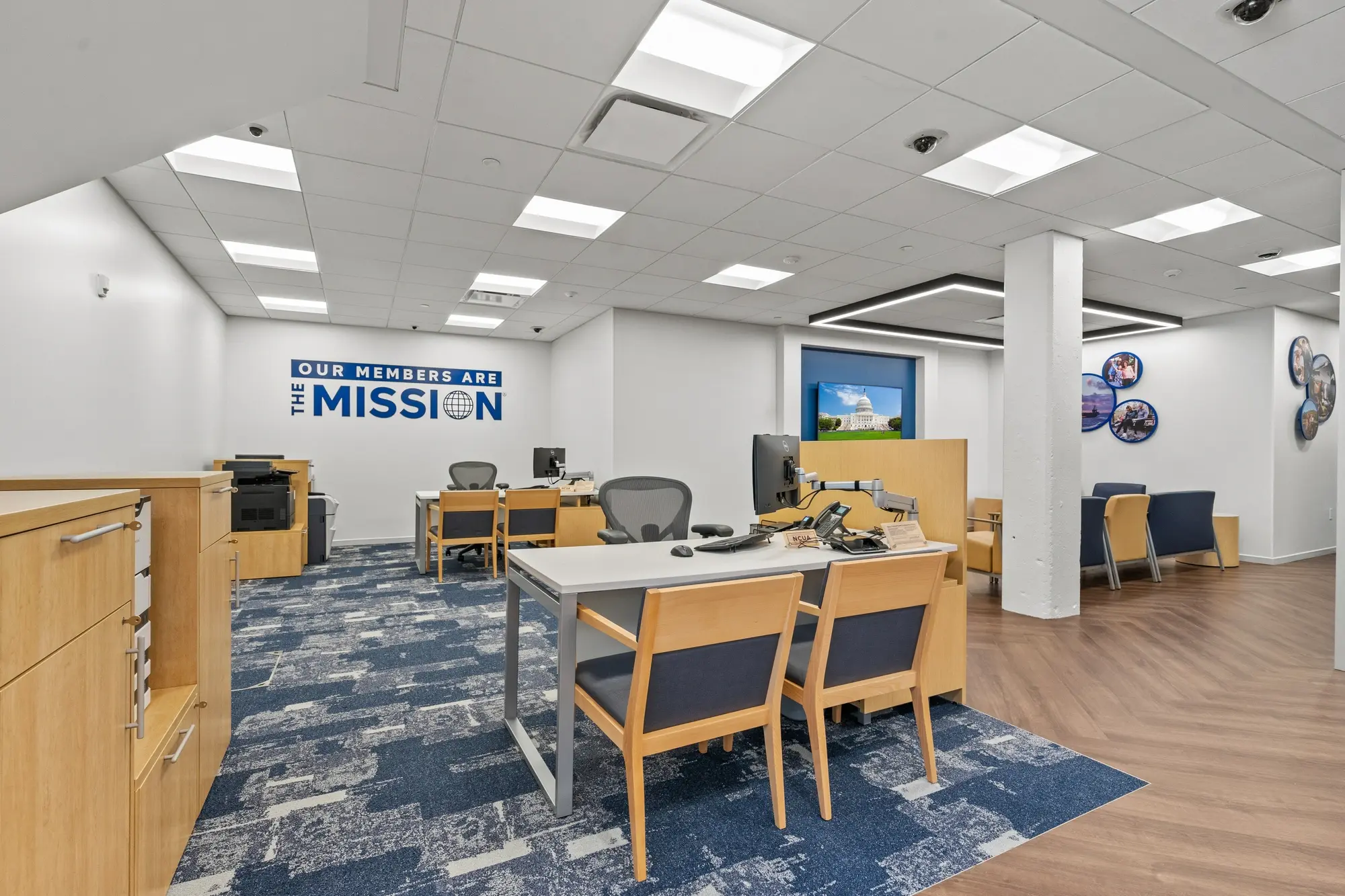 Member service area with advisor desks, ergonomic chairs, branded mission wall graphic, and blue patterned carpet