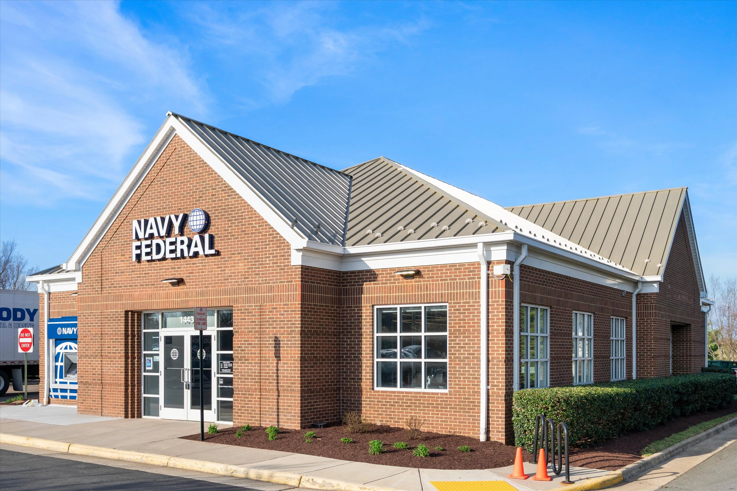 Navy Federal Credit Union Chantilly branch side angle showing brick exterior, metal roof, hedges, and blue sky with clouds