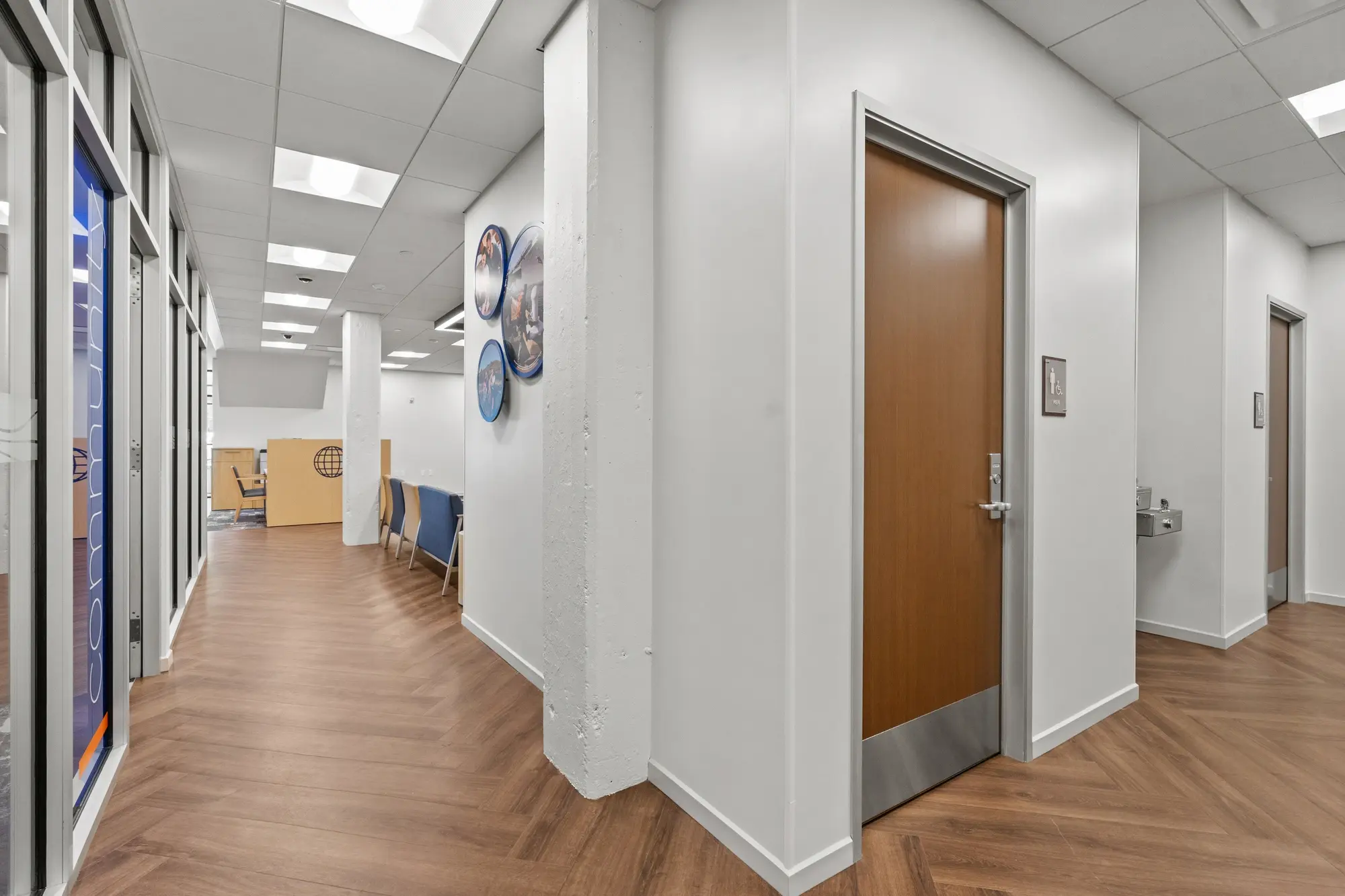 Branch hallway with herringbone flooring, restroom doors, water fountain, and circular branded artwork