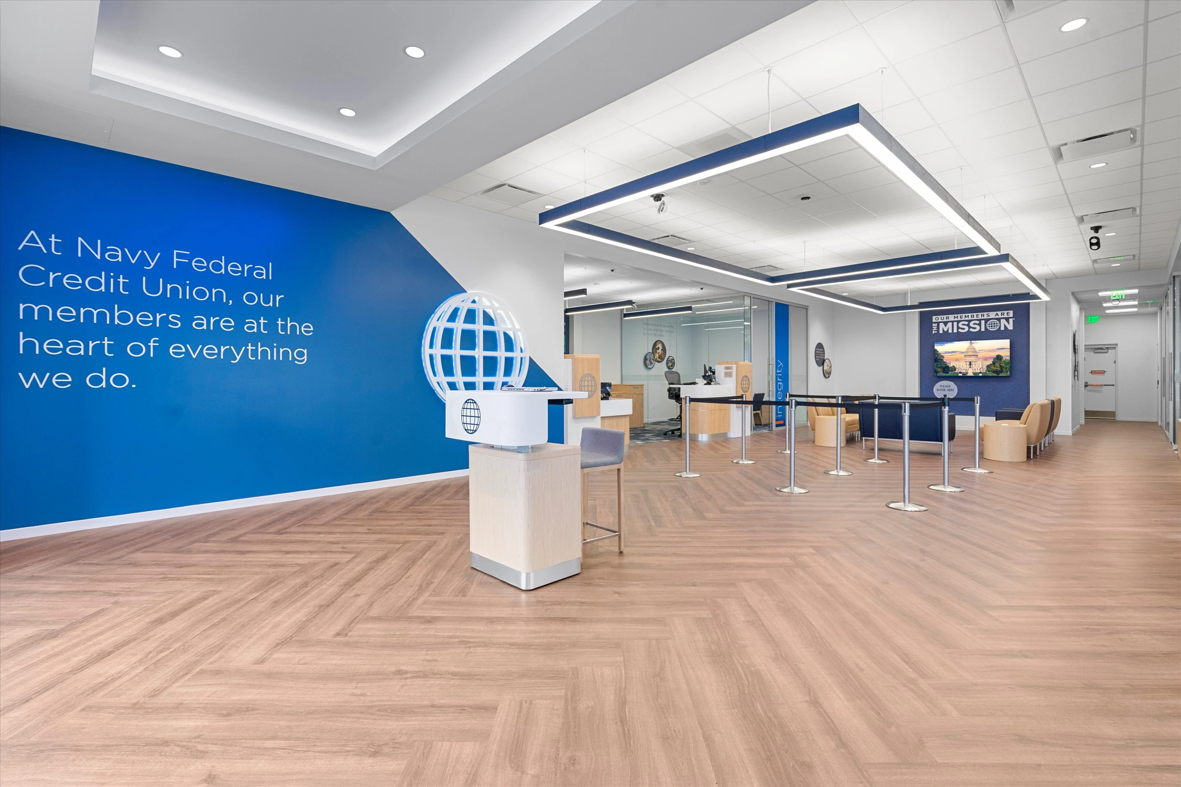 Main lobby featuring blue branded wall with "At Navy Federal Credit Union, our members are at the heart of everything we do" text, 3D globe logo, and greeter desk