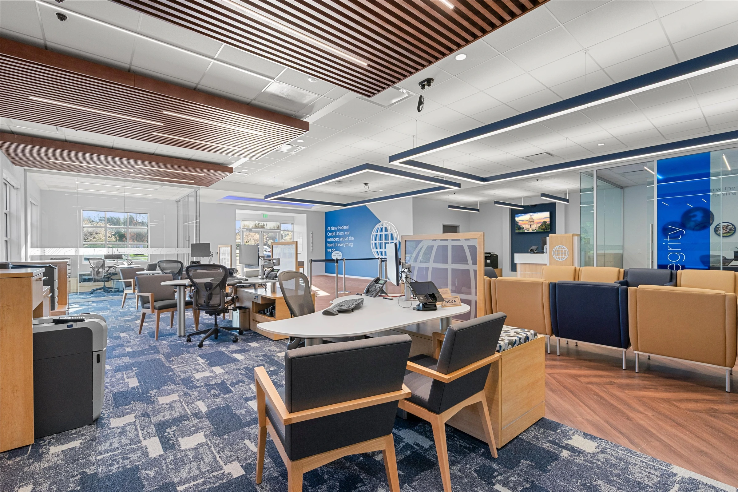 Open member service area with multiple advisor desks, wood slat ceiling, stanchion queue, "Our Members Are The Mission" display, and natural window light