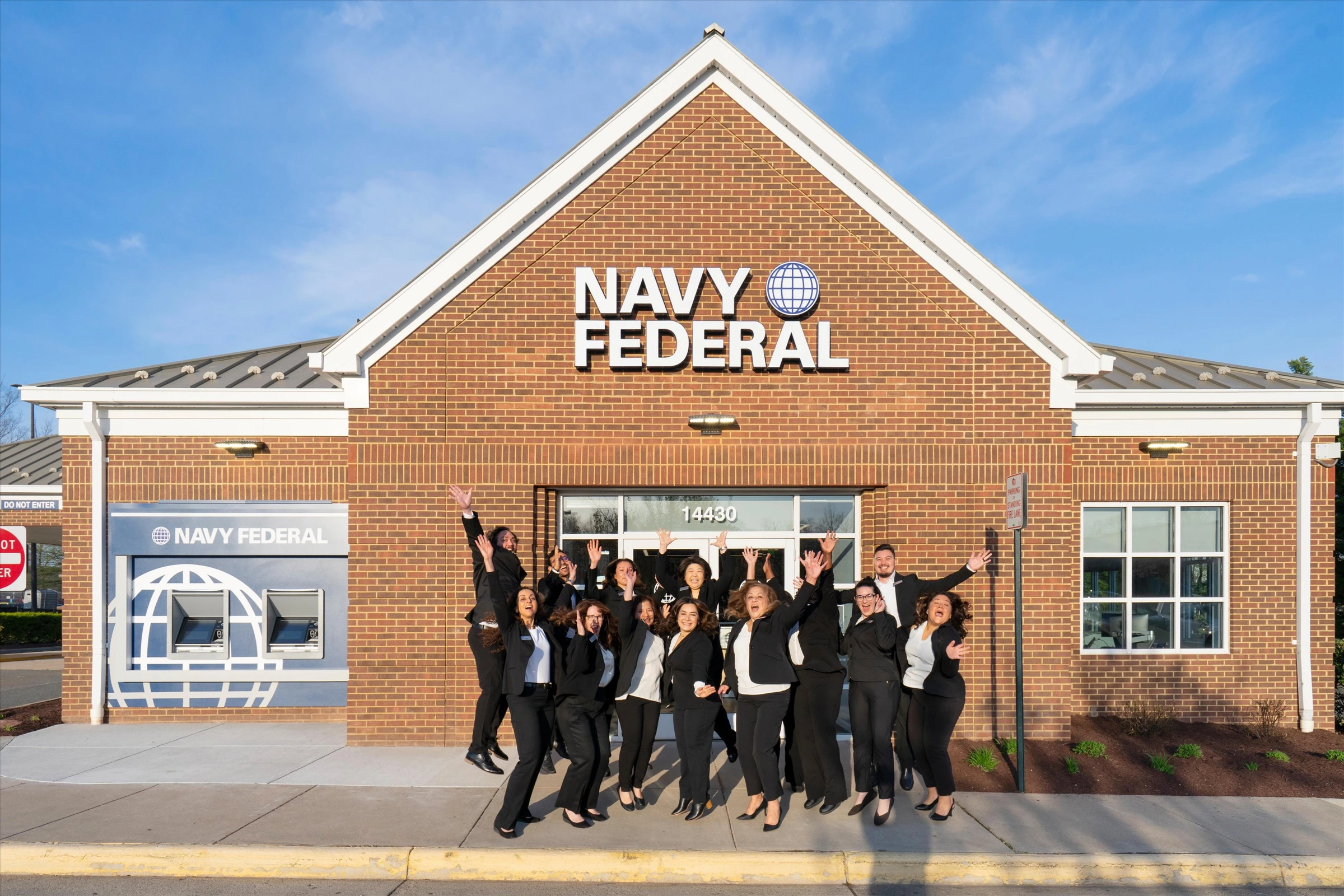 Navy Federal Credit Union Chantilly branch team celebrating outside the branch entrance with hands raised in front of brick facade and globe logo