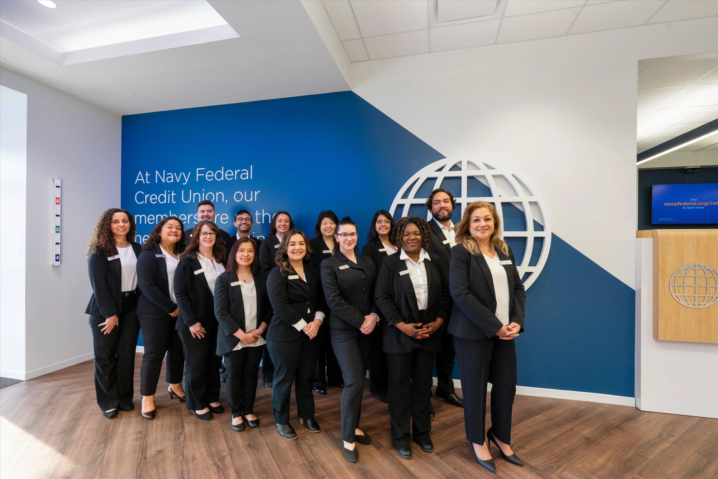 Navy Federal Credit Union Chantilly branch team group photo in entry lobby next to branded blue wall with "At Navy Federal" mission statement and 3D globe logo