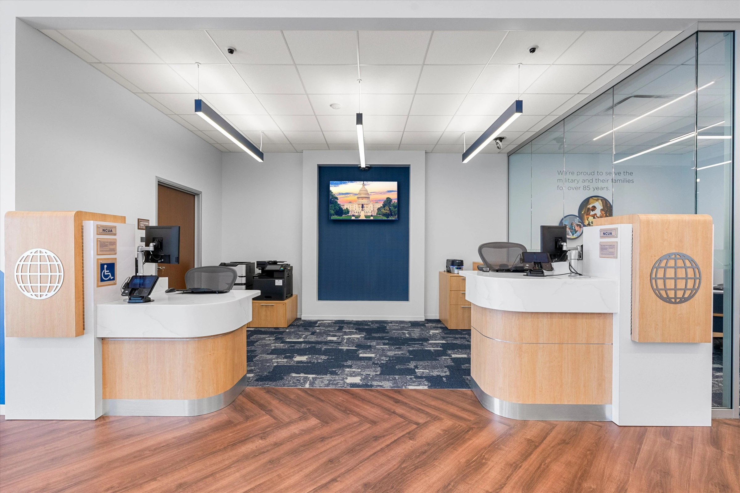 Dual teller stations with curved oak and white counters, globe logo panels, Capitol Building display on navy accent wall, and glass office partition