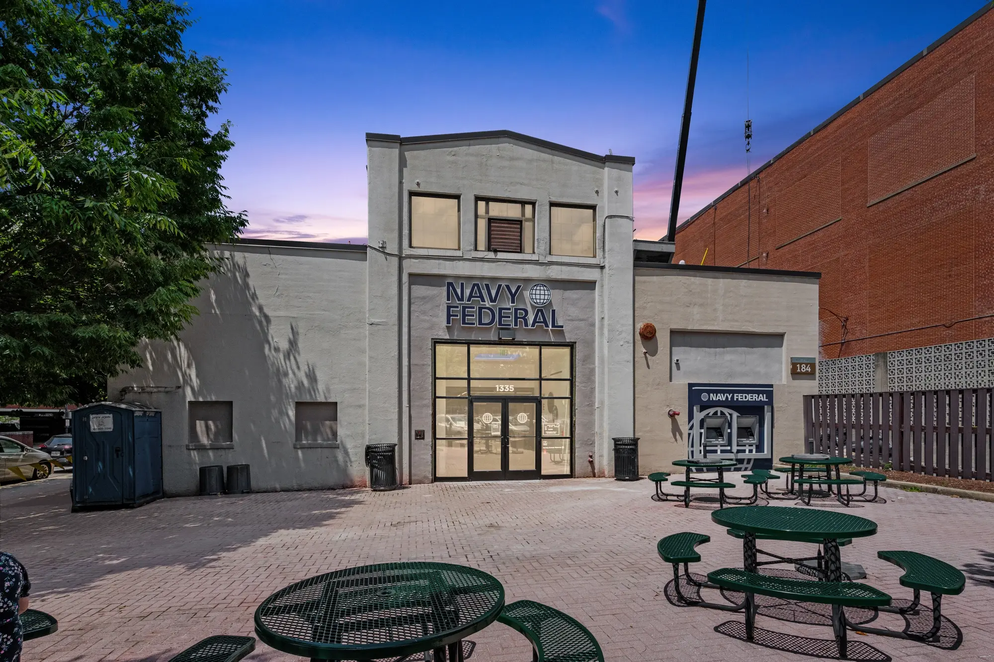 Navy Federal Credit Union branch exterior at twilight with illuminated signage, outdoor seating, and ATM kiosk in Washington DC