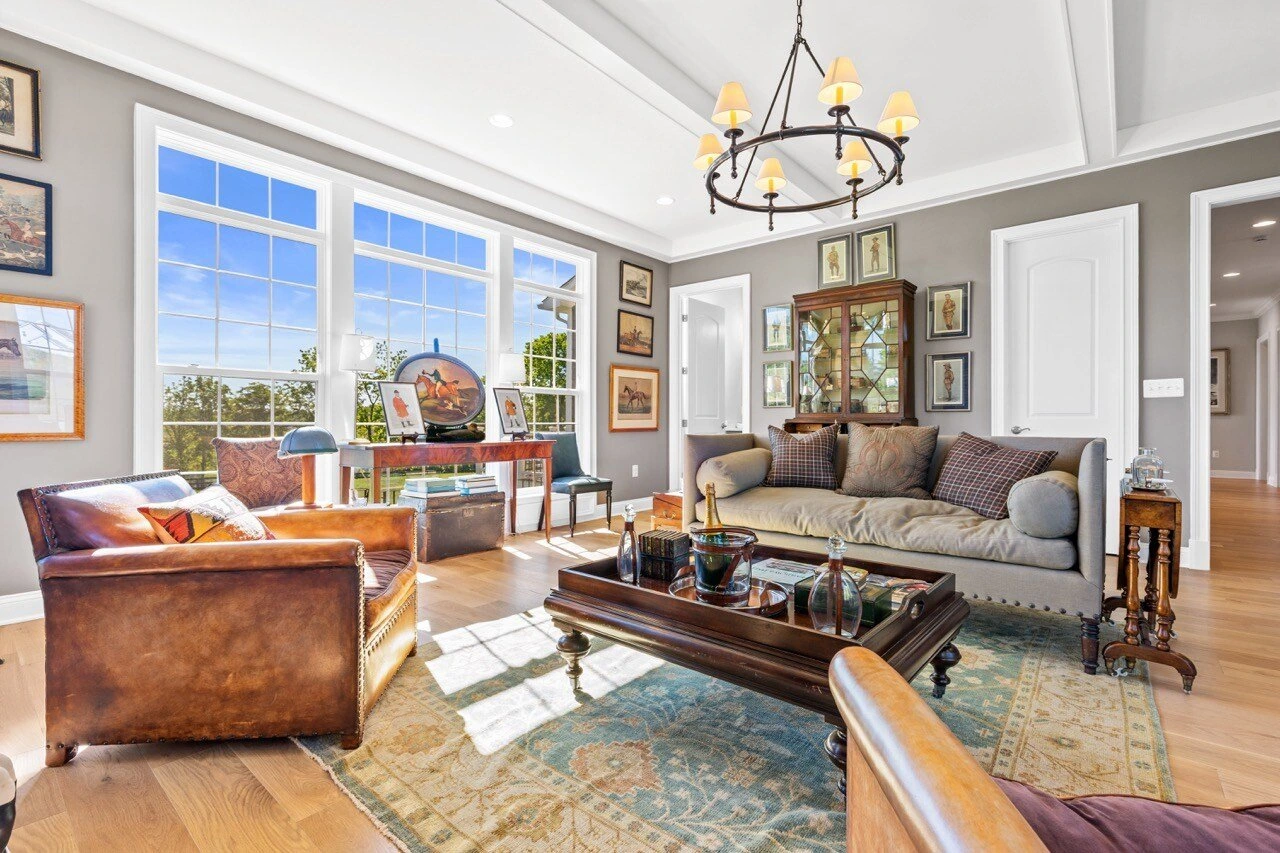 Sunlit living room with leather armchair, iron chandelier, and countryside views through large windows