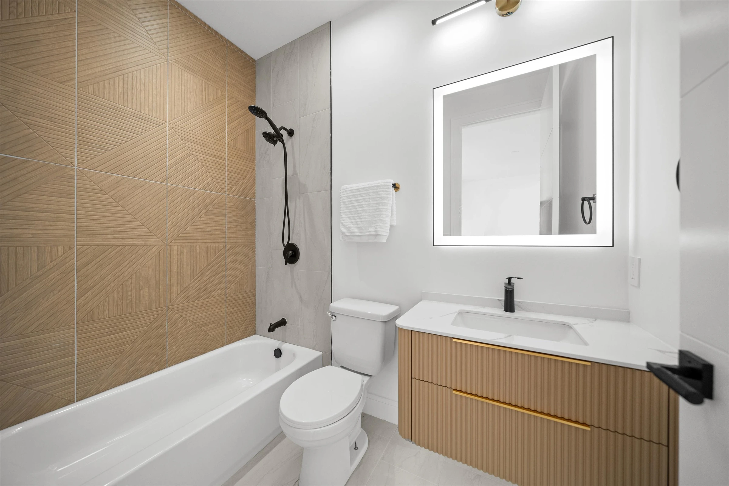 Bathroom with geometric wood-accent tile, bathtub-shower combo, LED backlit mirror, floating oak vanity, and matte black fixtures