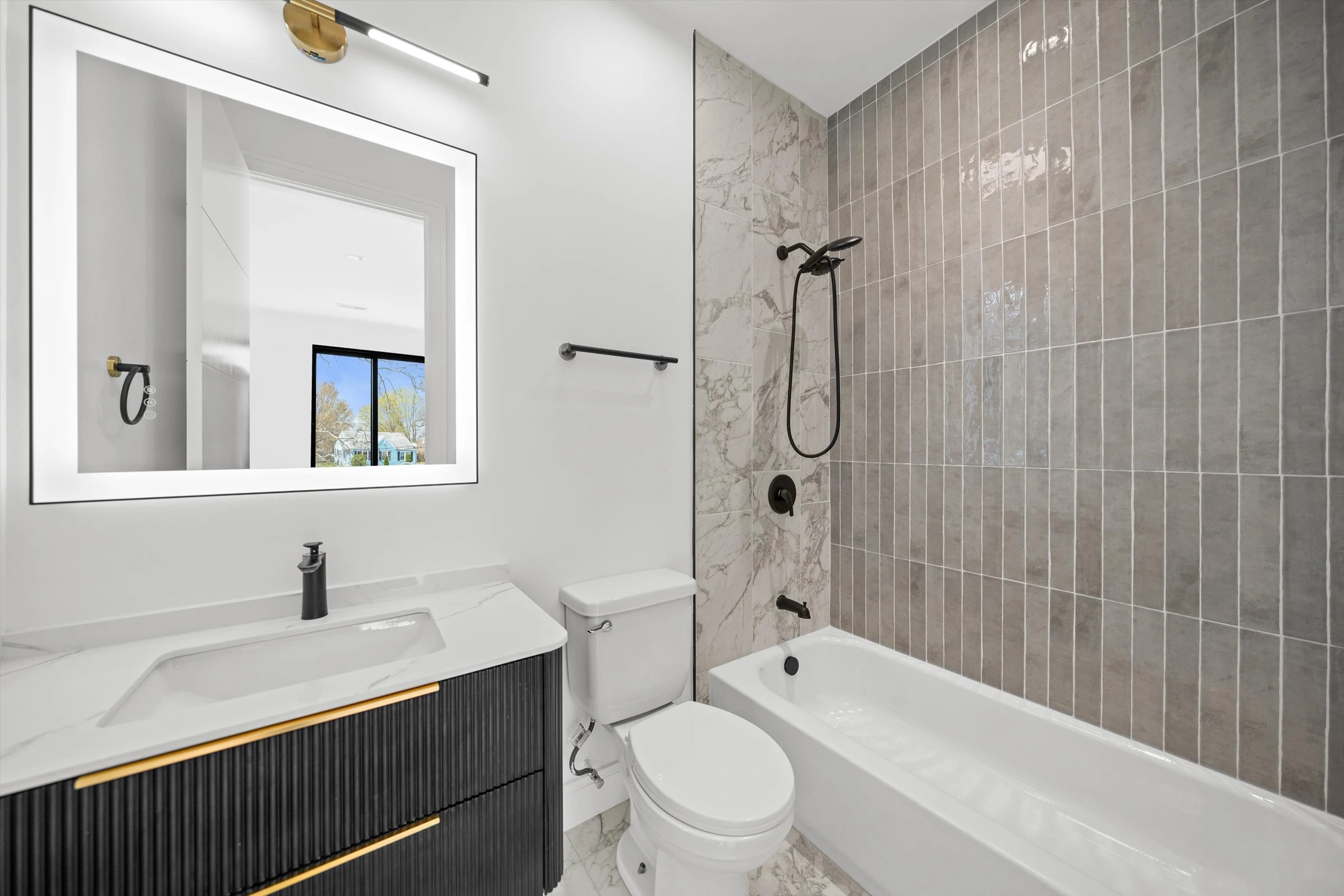 Bathroom with gray marble tile shower-tub combo, LED backlit mirror, dark fluted floating vanity with gold accent, and matte black fixtures