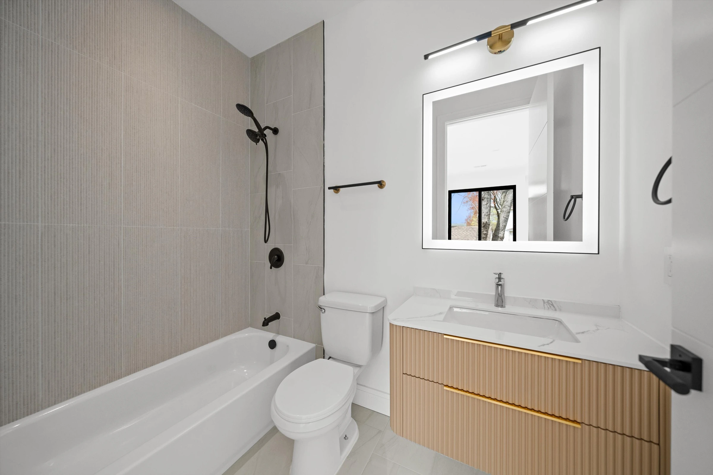 Bathroom with gray linear tile shower-tub combo, LED mirror, floating oak vanity with gold accent strip, and chrome faucet