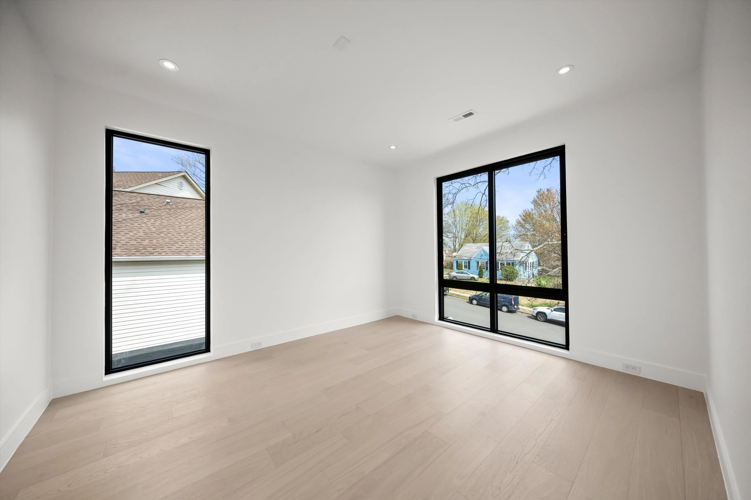 Third bedroom with two large black-framed windows, light oak floors, recessed lighting, and neighborhood views