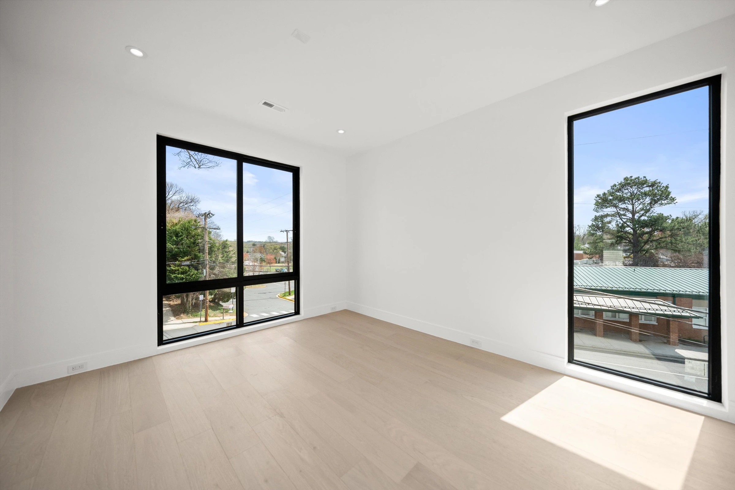 Fourth bedroom with floor-to-ceiling corner windows, light oak hardwood floors, and views of trees and rooftops